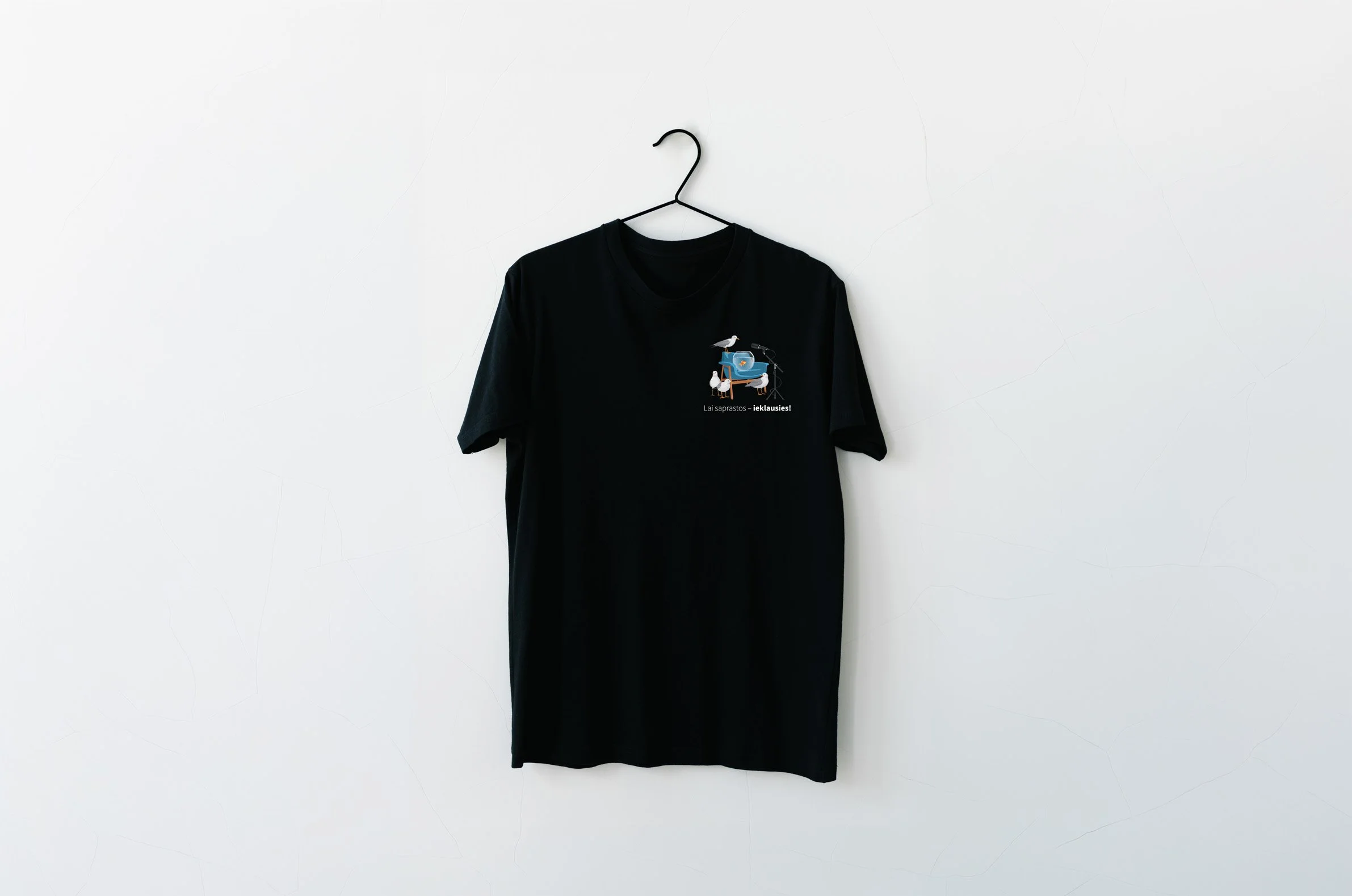 A black T-shirt hanging on a black hanger against a plain white wall. The T-shirt features a graphic design of birds and a small boat with text below it.