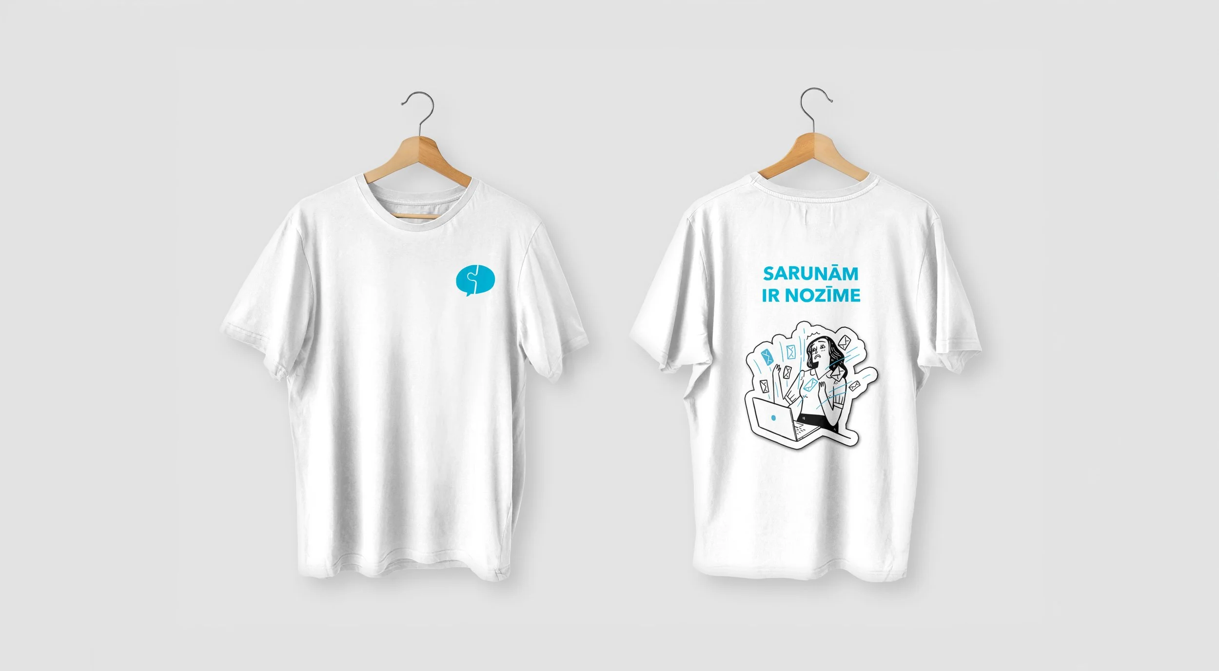 Two white T-shirts on hangers against a plain background, one with a blue speech bubble logo on the front and the other with a colorful graphic of a woman working at a laptop with floating icons and the text "SARUNĀM IR NOZĪME" above.