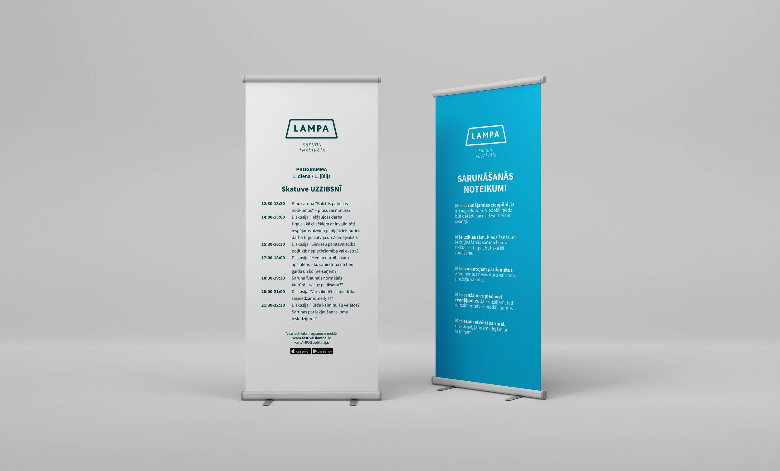 Two standing banners display event information and guidelines for a festival named 'Lampa.' The left banner is white with blue and black text, listing schedule details in Latvian. The right banner is blue with white text, providing festival rules and guidelines.