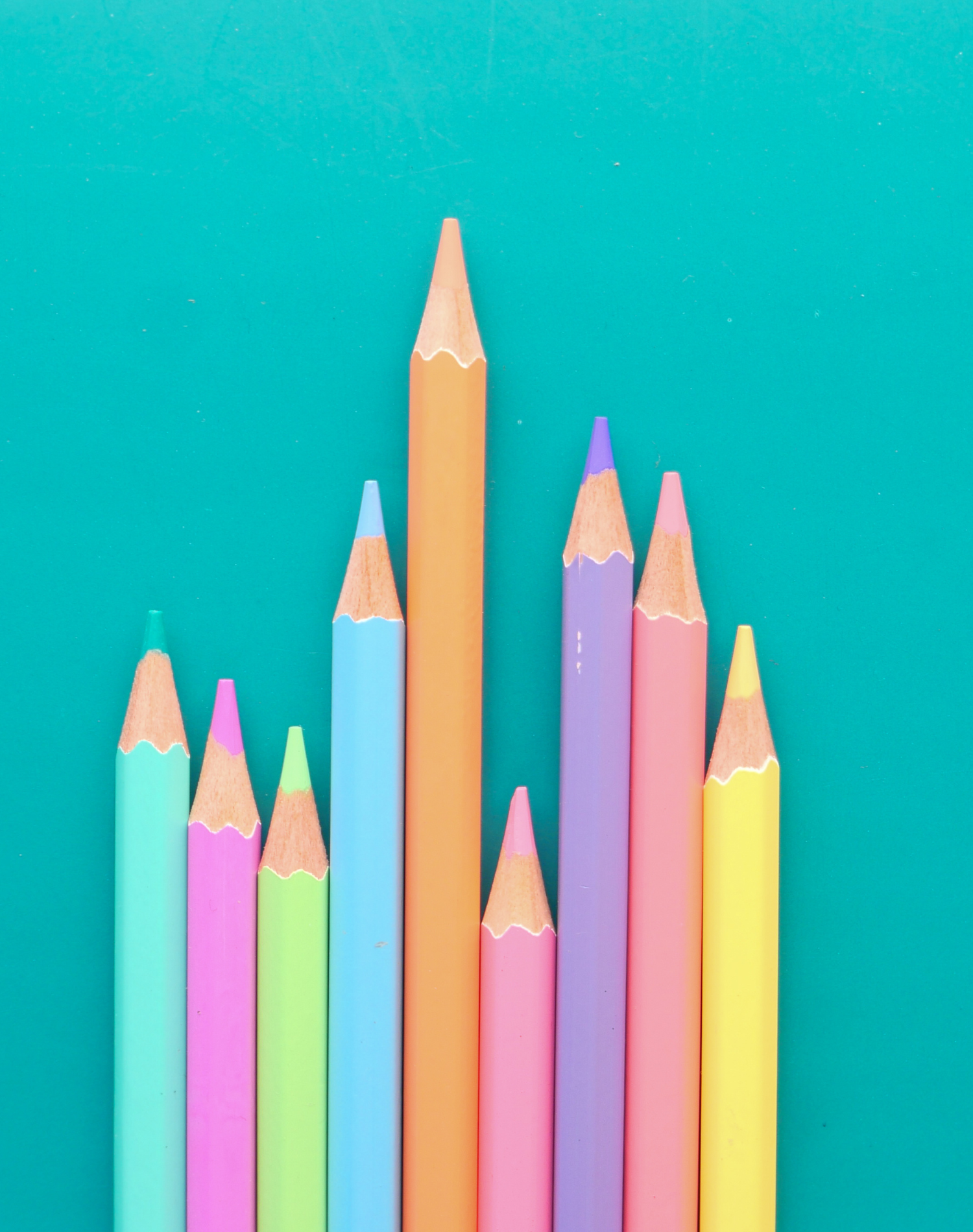 A colorful set of pencil-shaped crayons arranged vertically on a teal background, with the longest crayon in the center.
