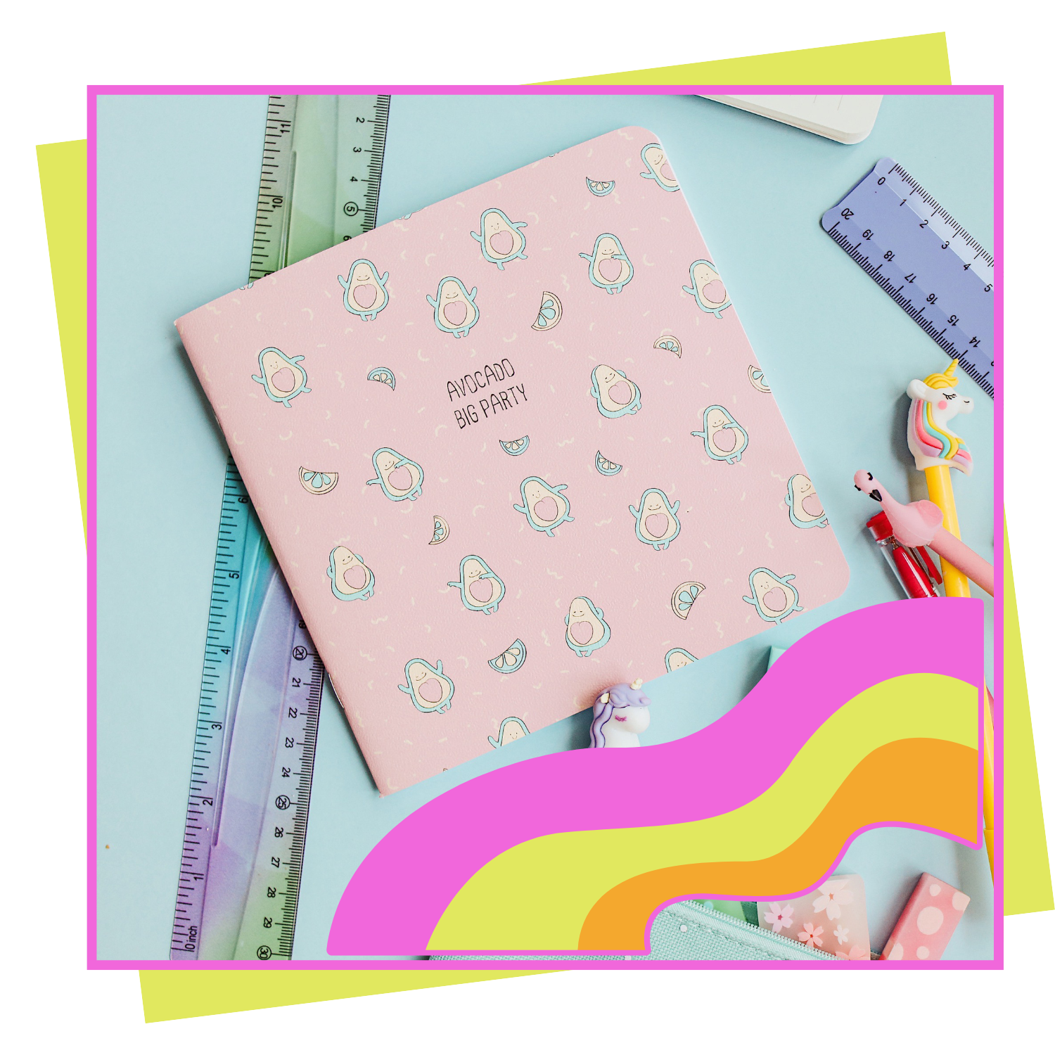 A pink notebook with avocado illustrations and the text "AVOCADO BIG PARTY" on the cover, surrounded by rulers, pens, and unicorn-shaped stationery on a light blue background with lime green and pink border accents.