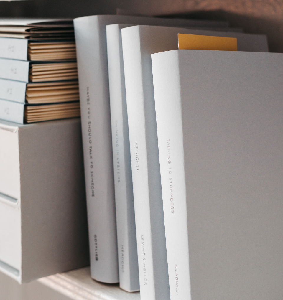 A collection of opened and closed books and magazines on a shelf, with visible titles like "Talking to Strangers" and "Attracted".