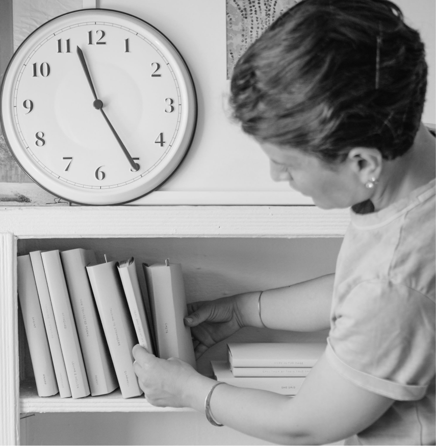 A woman looking at a row of books on a shelf, in black & white.