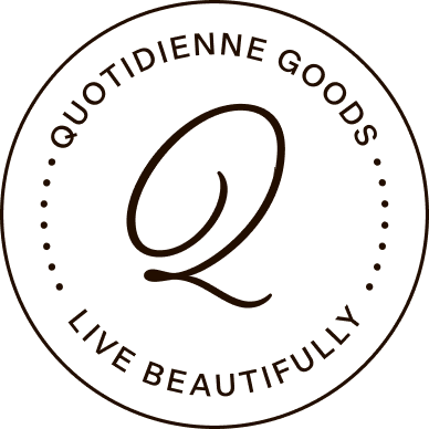 A circular logo with the text 'Quotidienne Goods' at the top and 'Live Beautifully' at the bottom, surrounding a stylized letter 'Q' in the center.