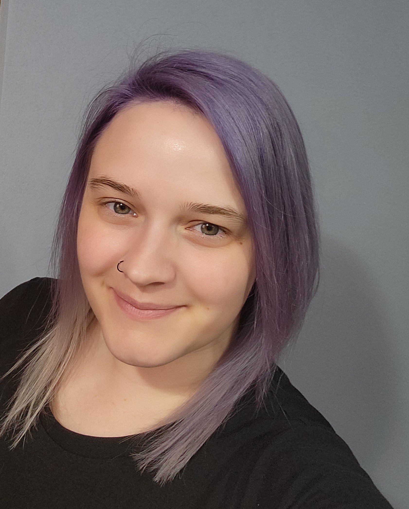 Close-up of a woman's face with purple and brown hair, wearing a black shirt, and a small nose ring.
