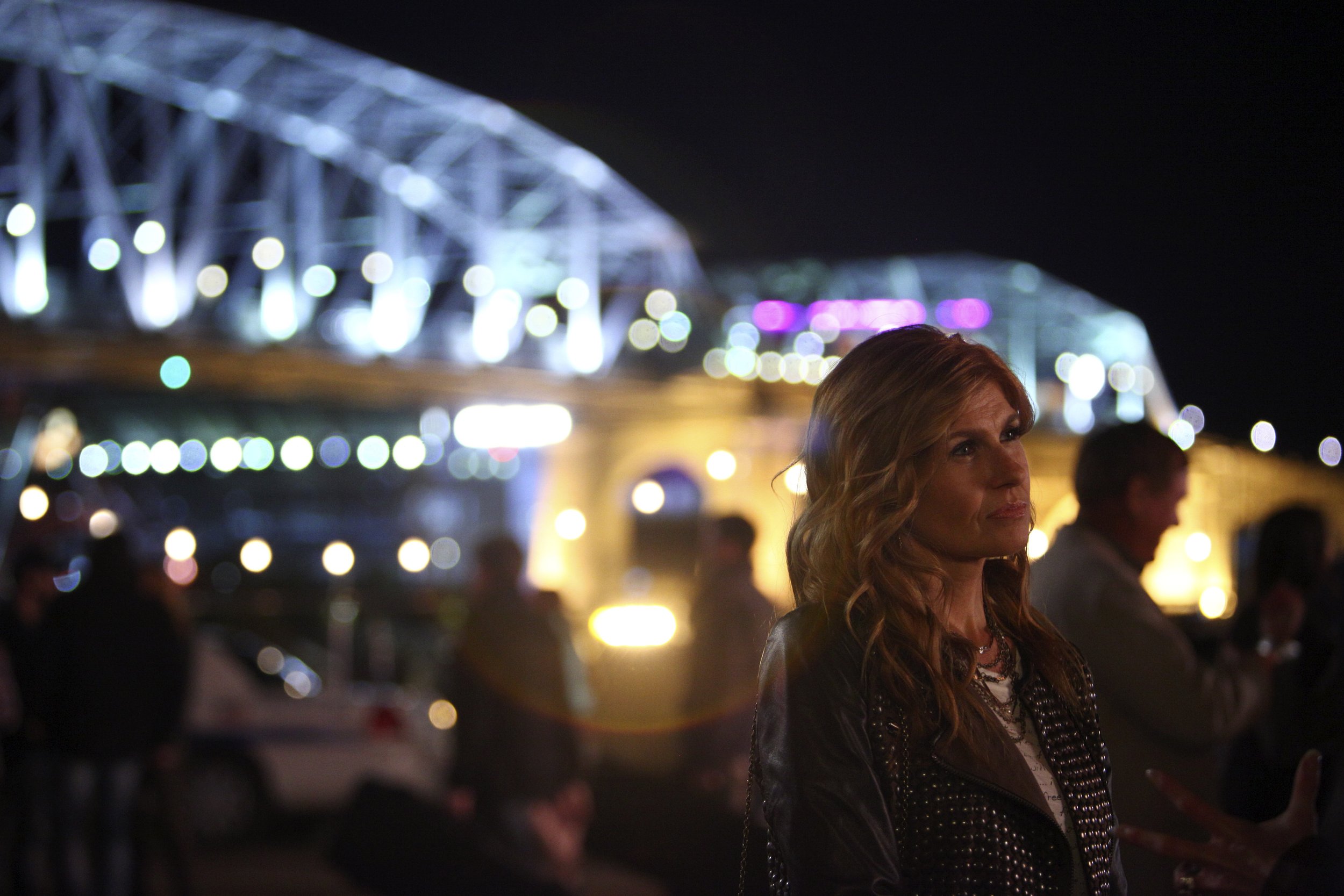 The Nashville tv show character Reyna James at night in front of a lit bridge with colorful lights.