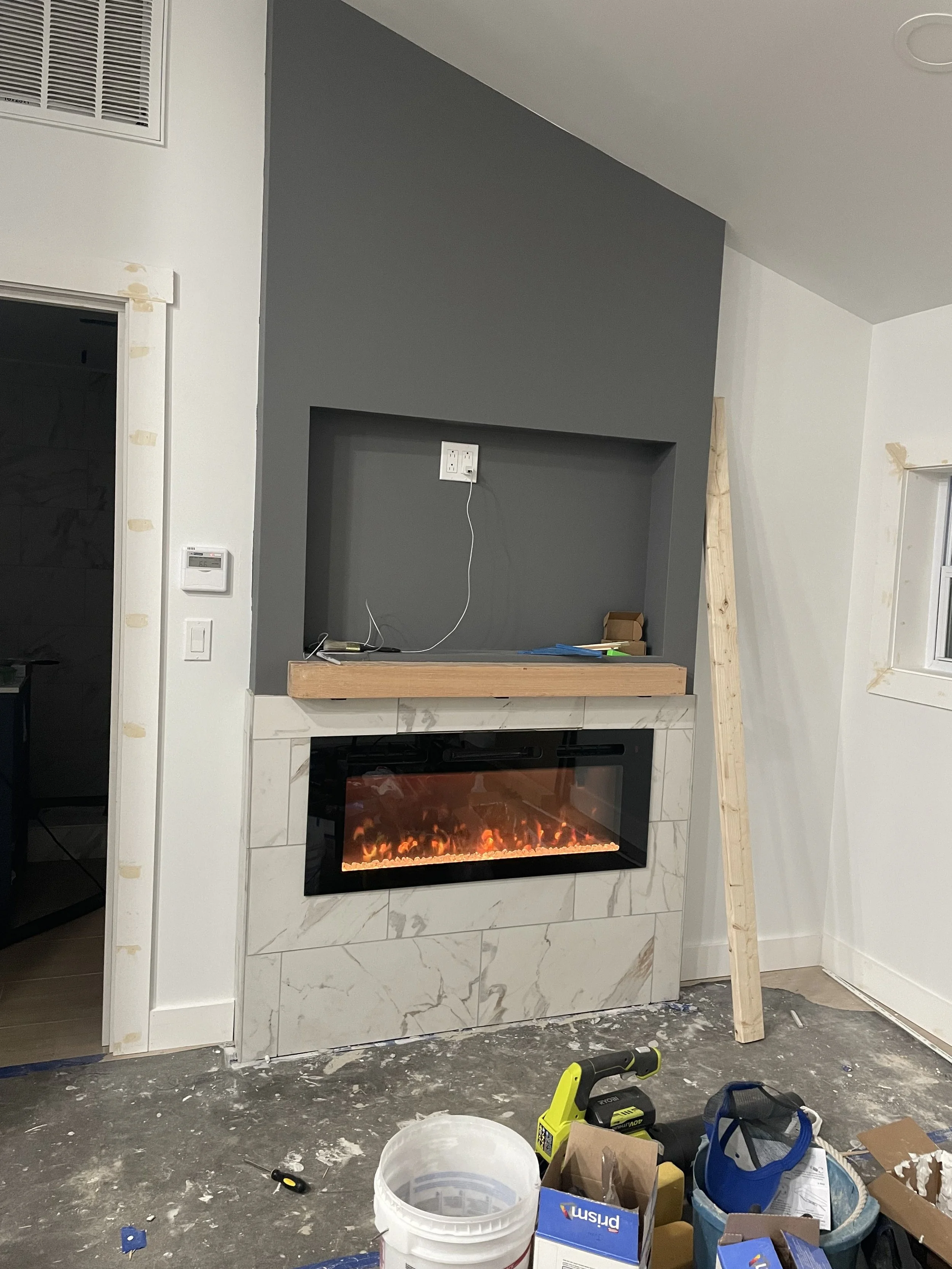 Living room with a modern fireplace, gray accent wall, and construction tools and materials scattered on the floor.