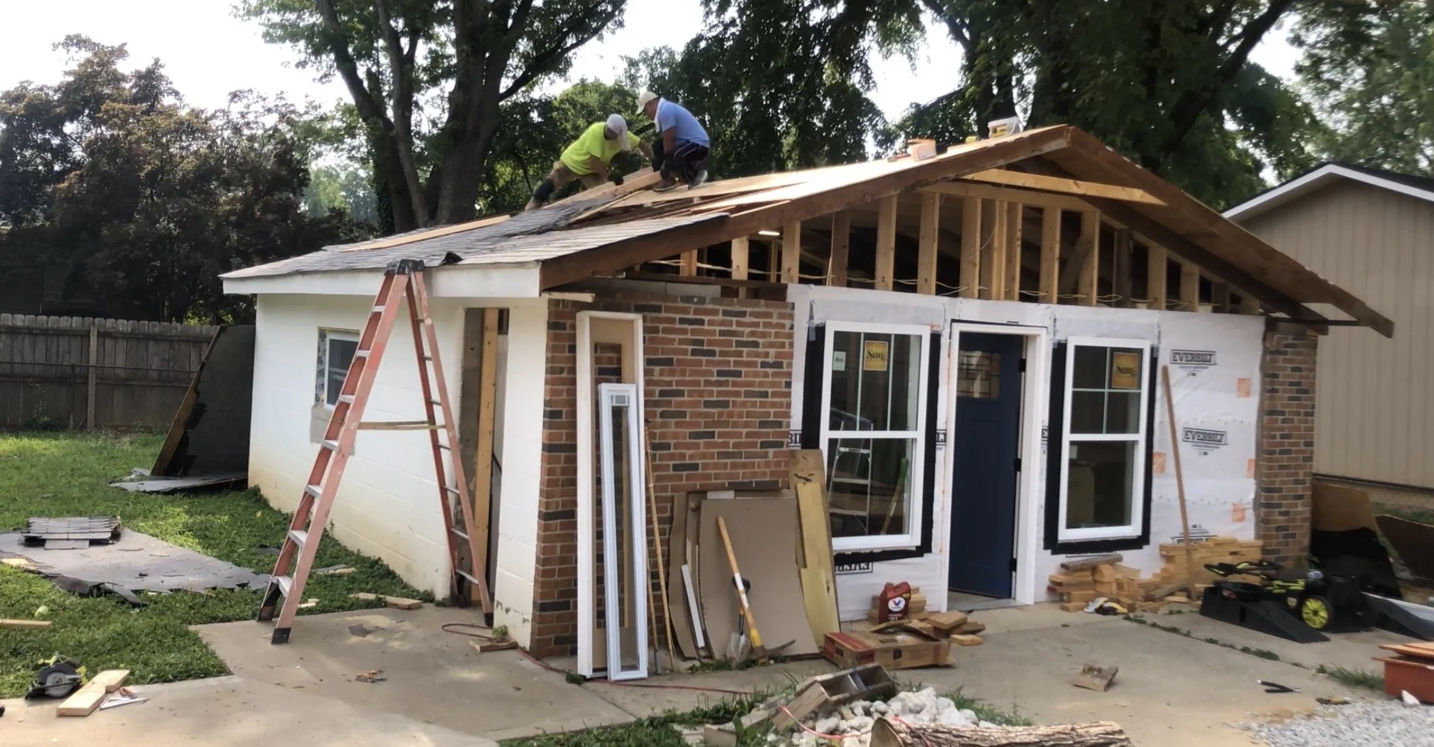 Construction workers on a roof working on a house renovation, with building materials and tools scattered around.