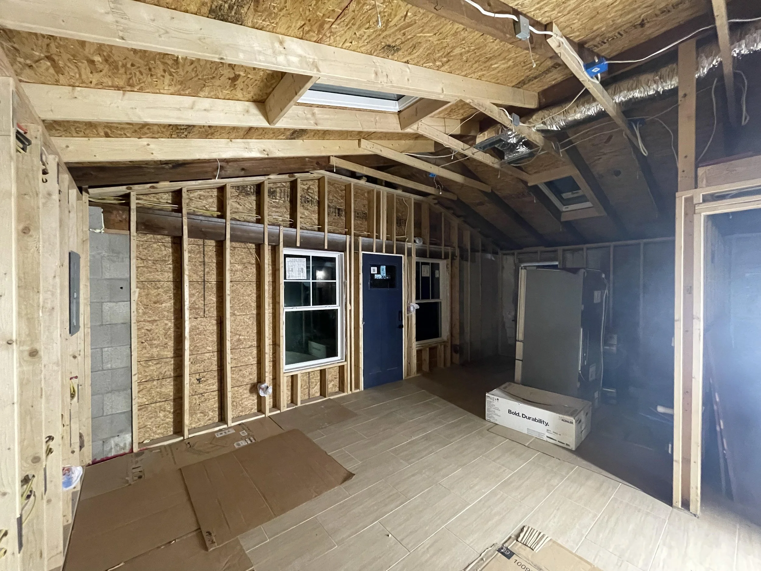 Interior of a house under construction with exposed wooden framing, insulation, electric wiring, and partially installed flooring.