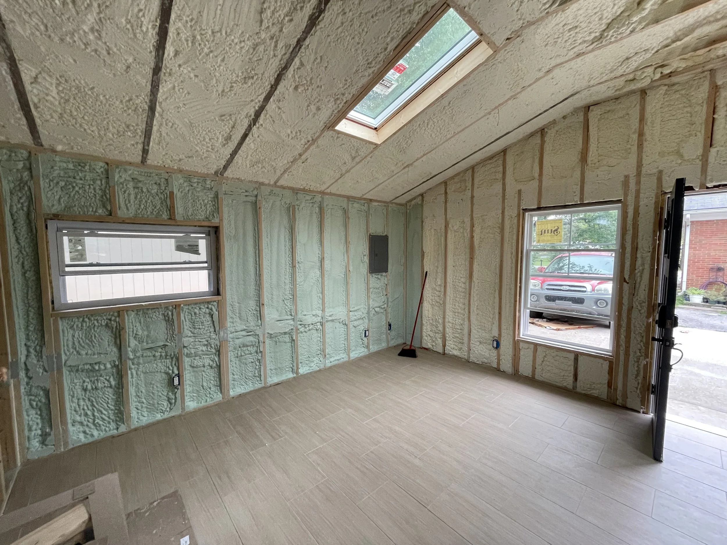 Interior view of a room under construction with drywall and spray foam insulation on the walls and ceiling, and a skylight window in the ceiling.