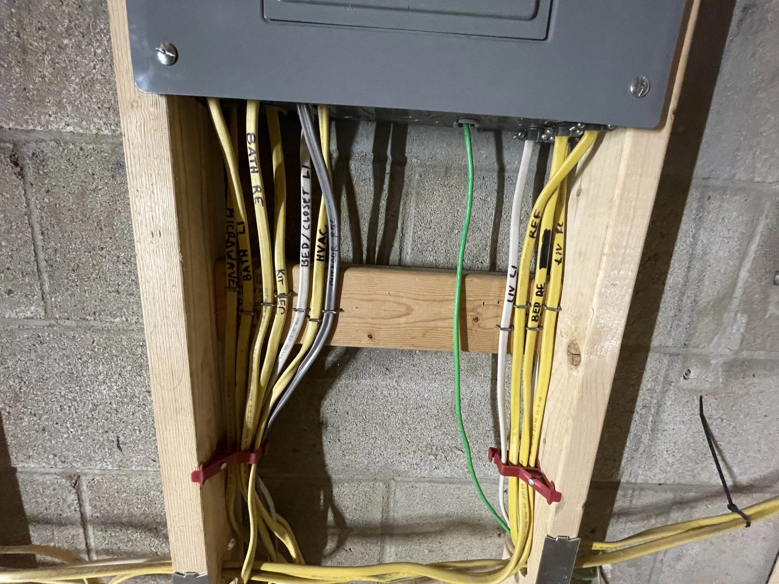 Electrical wires organized and secured on a wooden board mounted on a concrete wall.