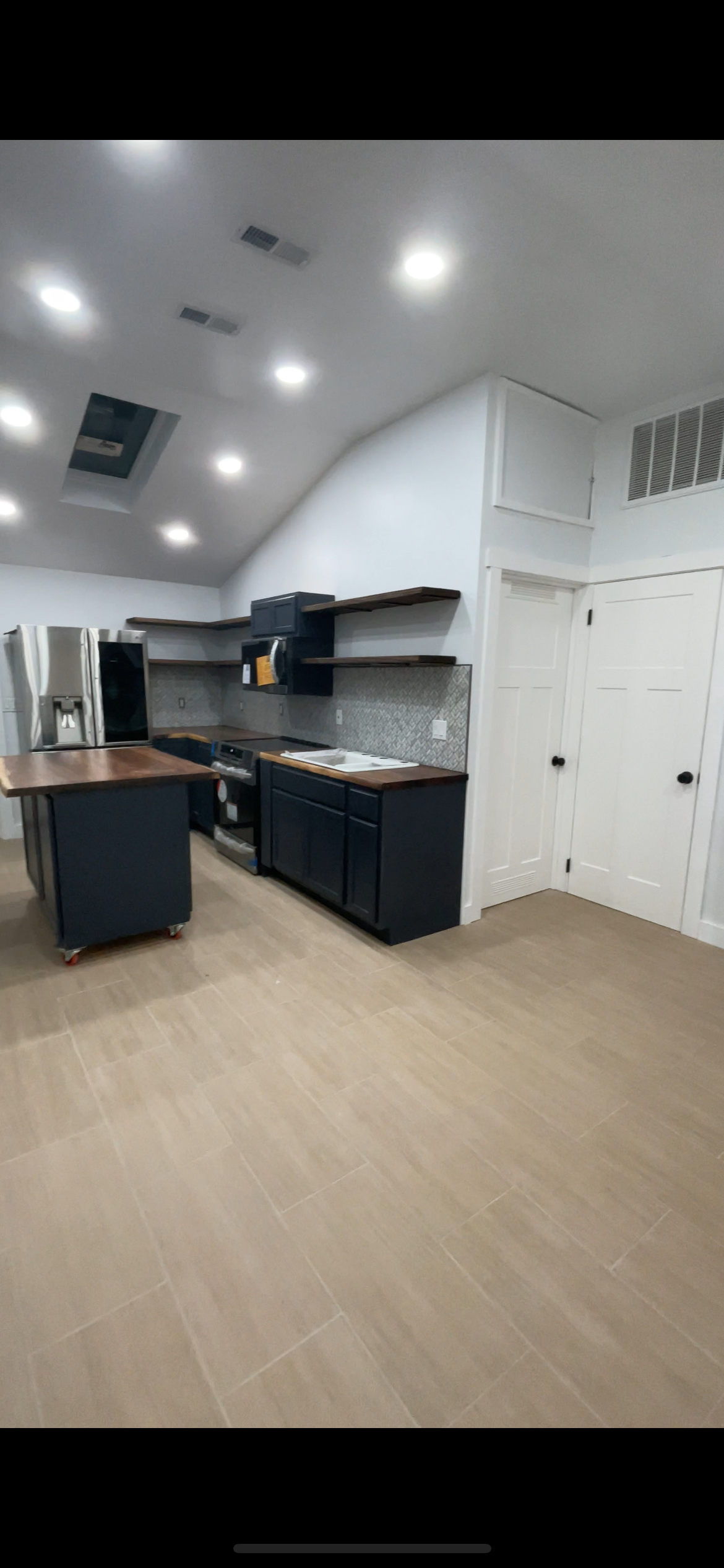 Modern kitchen with navy blue cabinets, wooden countertops, stainless steel appliances, open shelving, and beige tiled flooring.