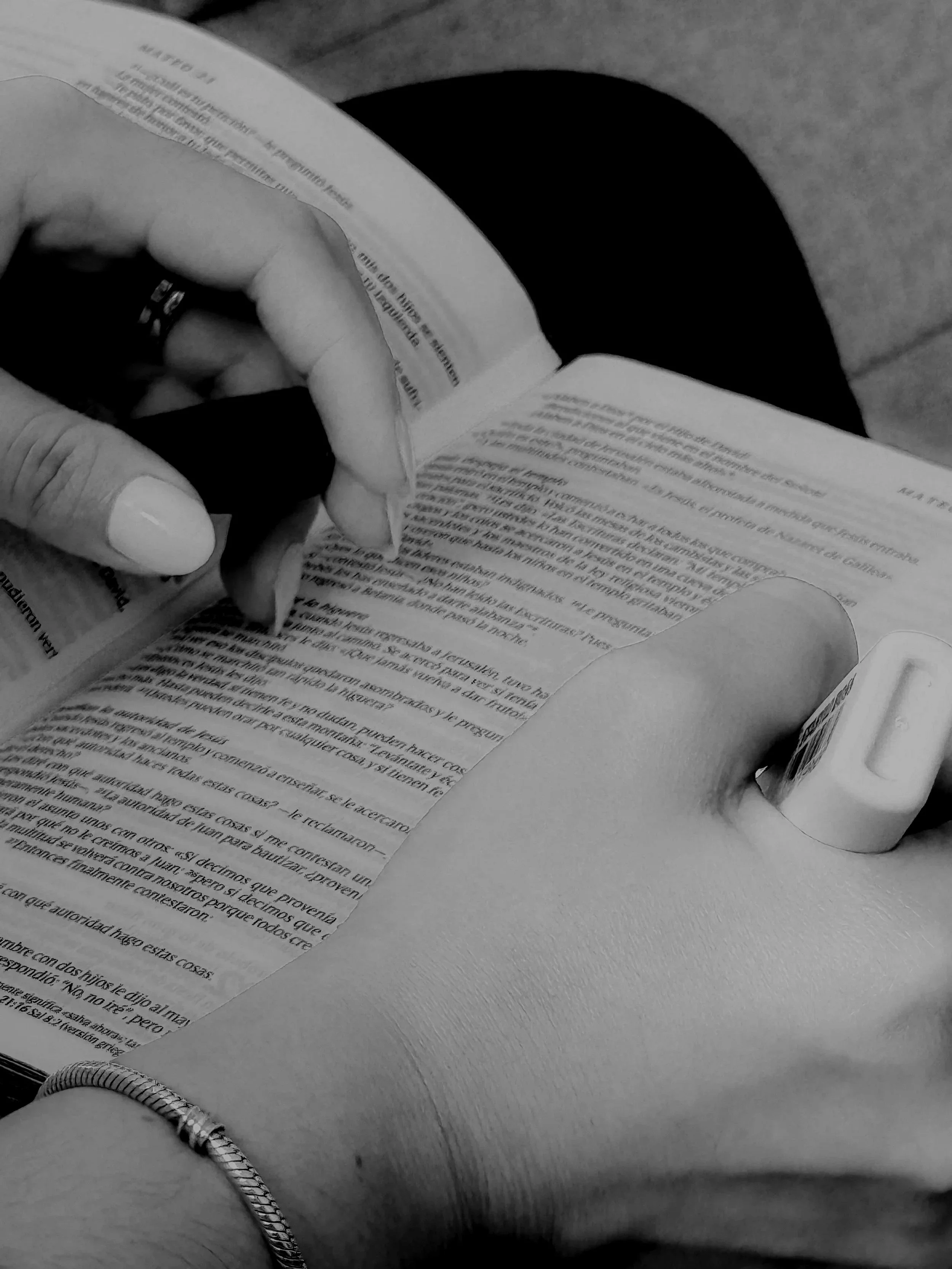 Persona leyendo un libro mientras está sentado, con un collar de cadena en la muñeca, en un entorno de superficie de madera.