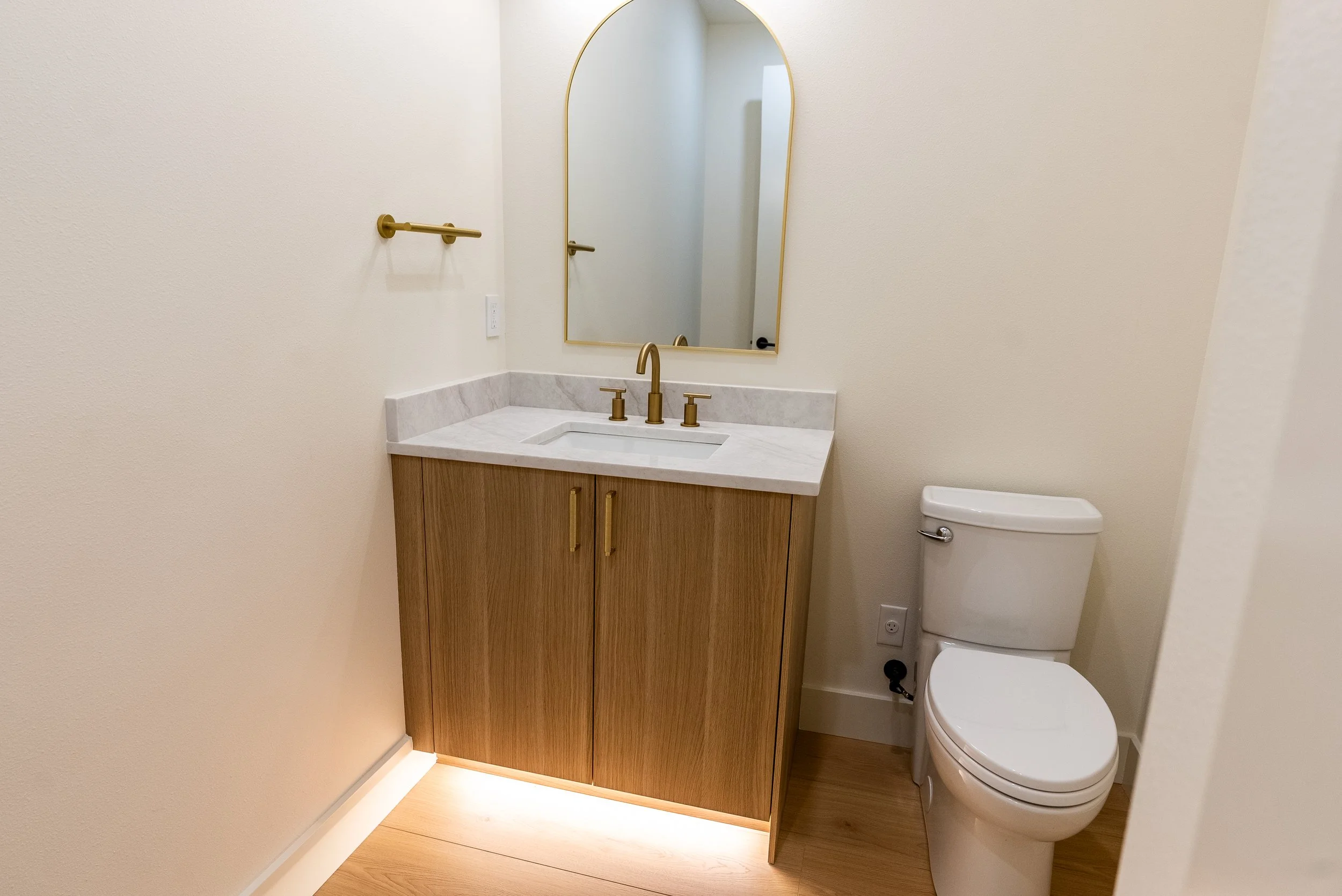 Bathroom with a white vanity with marble countertop, gold fixtures, a tall mirror, and a white toilet next to the vanity.