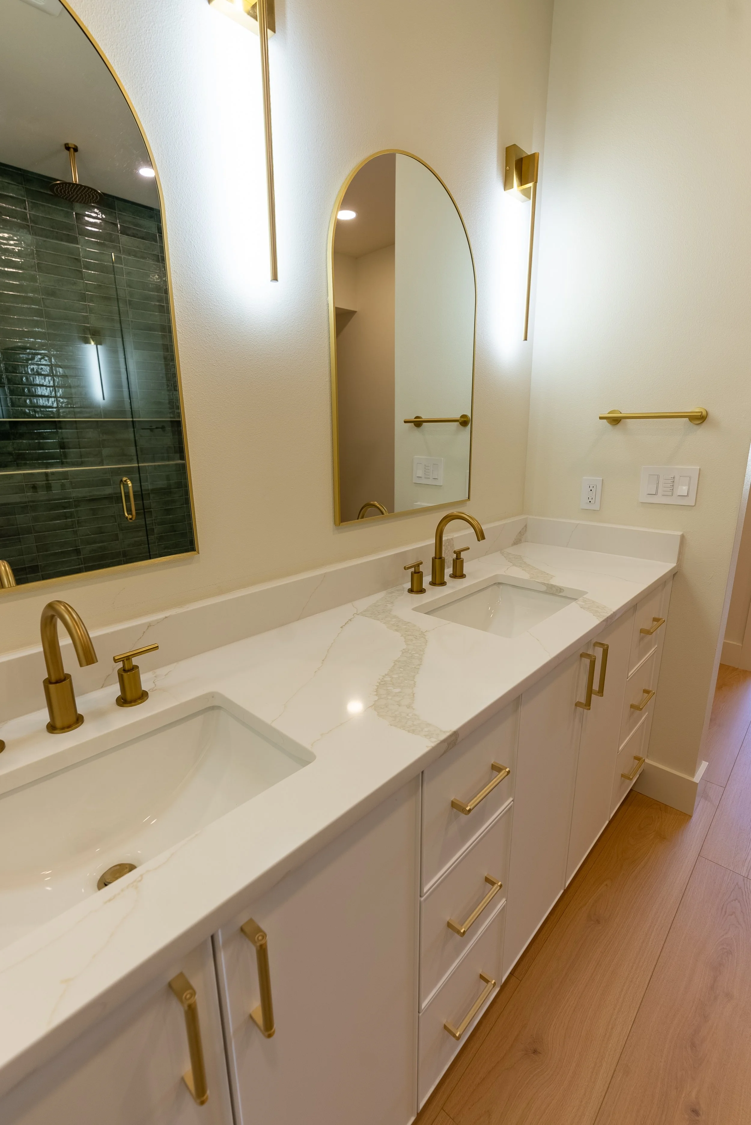 Bathroom vanity with two sinks, gold fixtures, white marble countertop, large mirror, and beige walls.