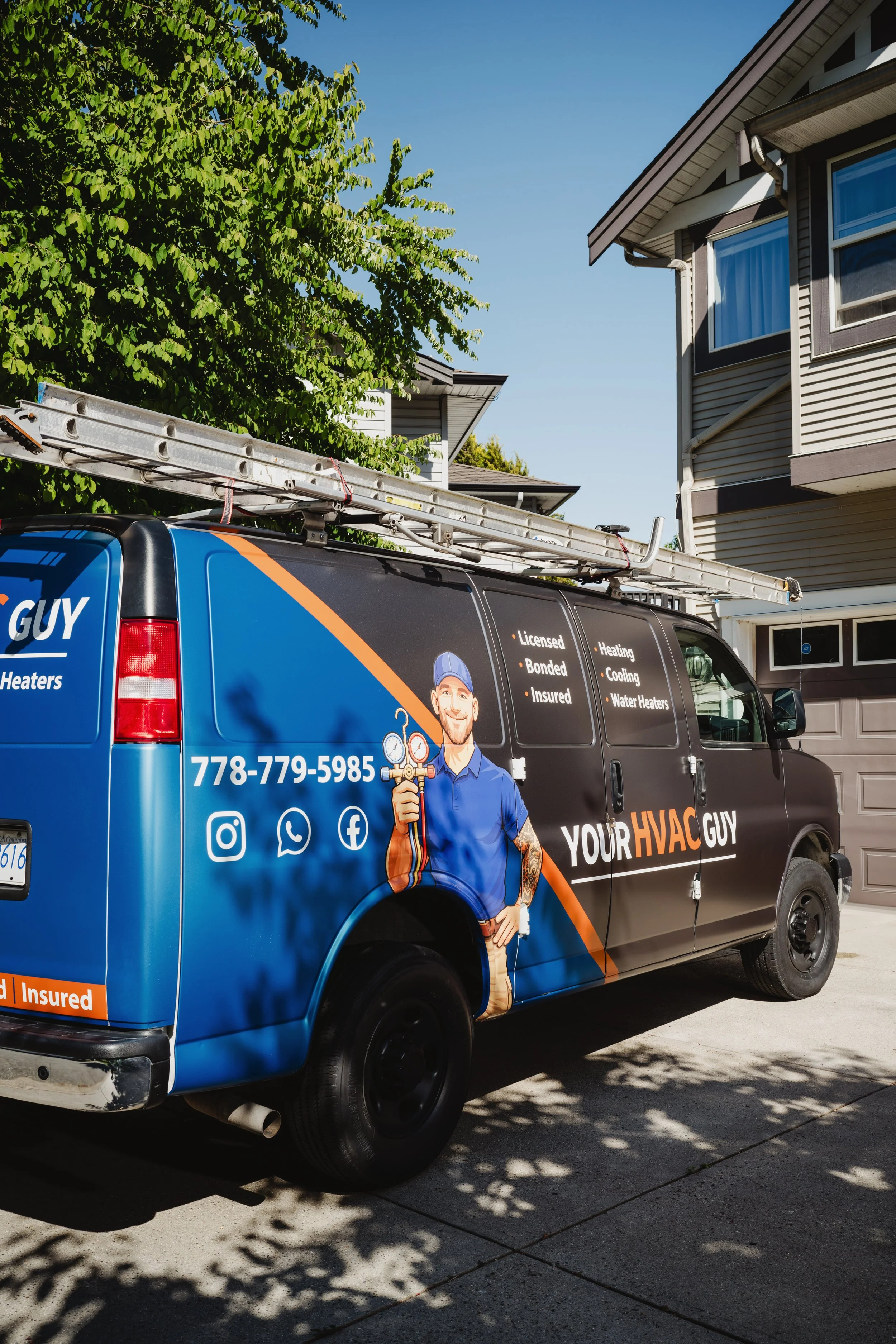 A black service van with advertising for HVAC services, parked in front of a residential house with trees and blue sky visible, featuring a ladder on top of the van and a cartoon image of a technician holding a wrench.