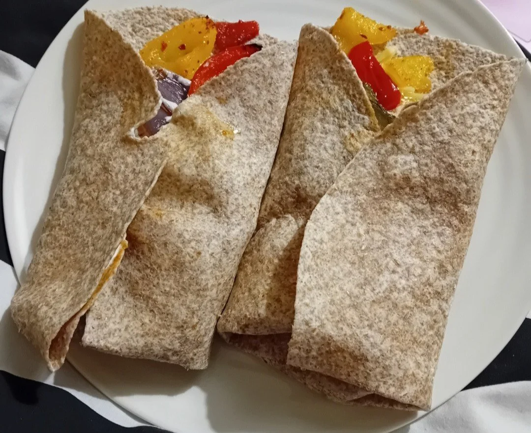 Two fajitas wrapped in wholemeal tortillas on a white plate, with visible yellow and red bell peppers inside.