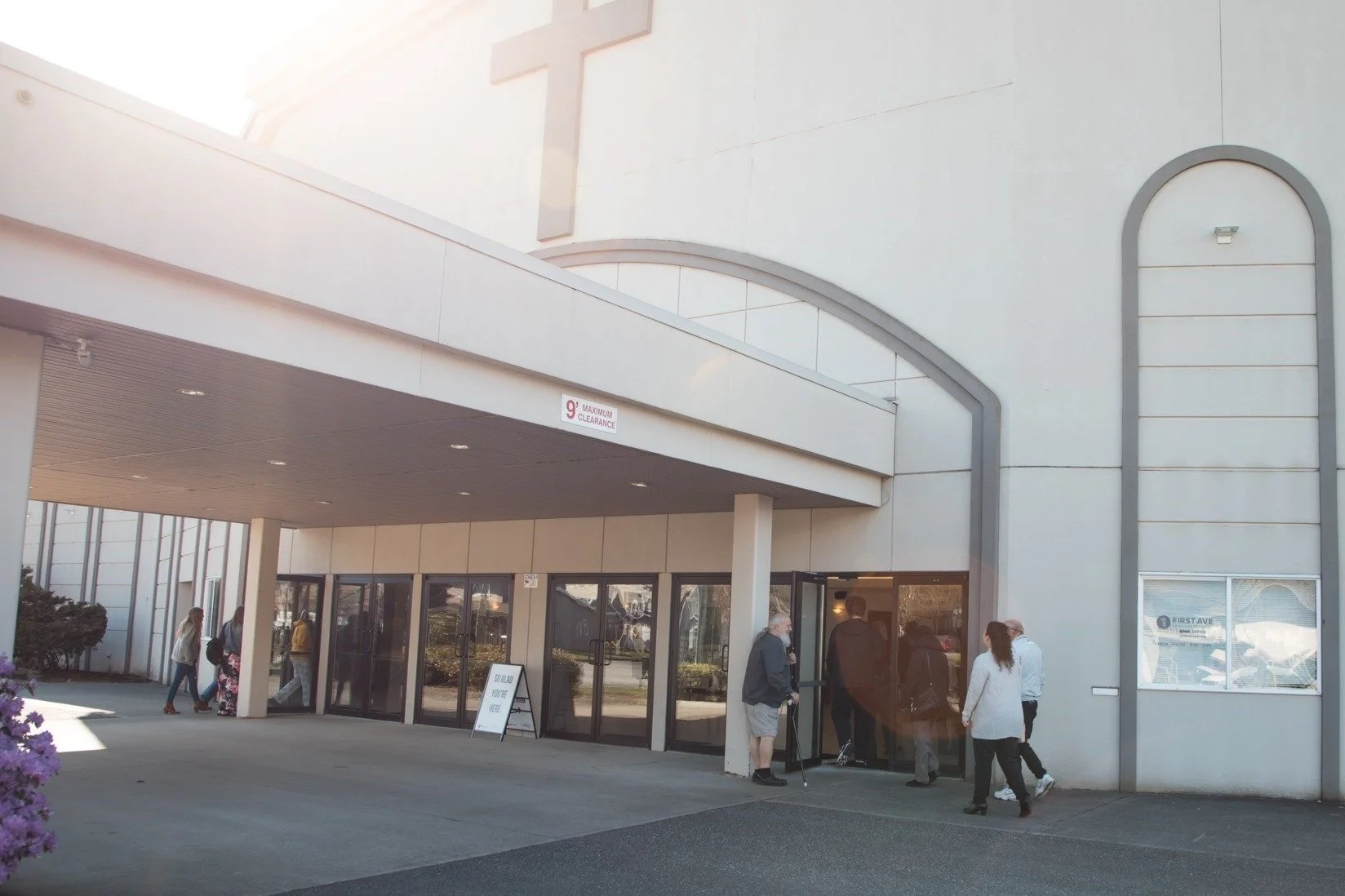 Front of church, people walking into building, sun beaming