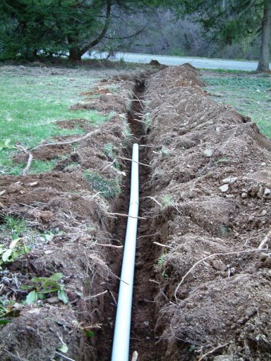 A trench dug in the ground with a white PVC pipe installed inside.