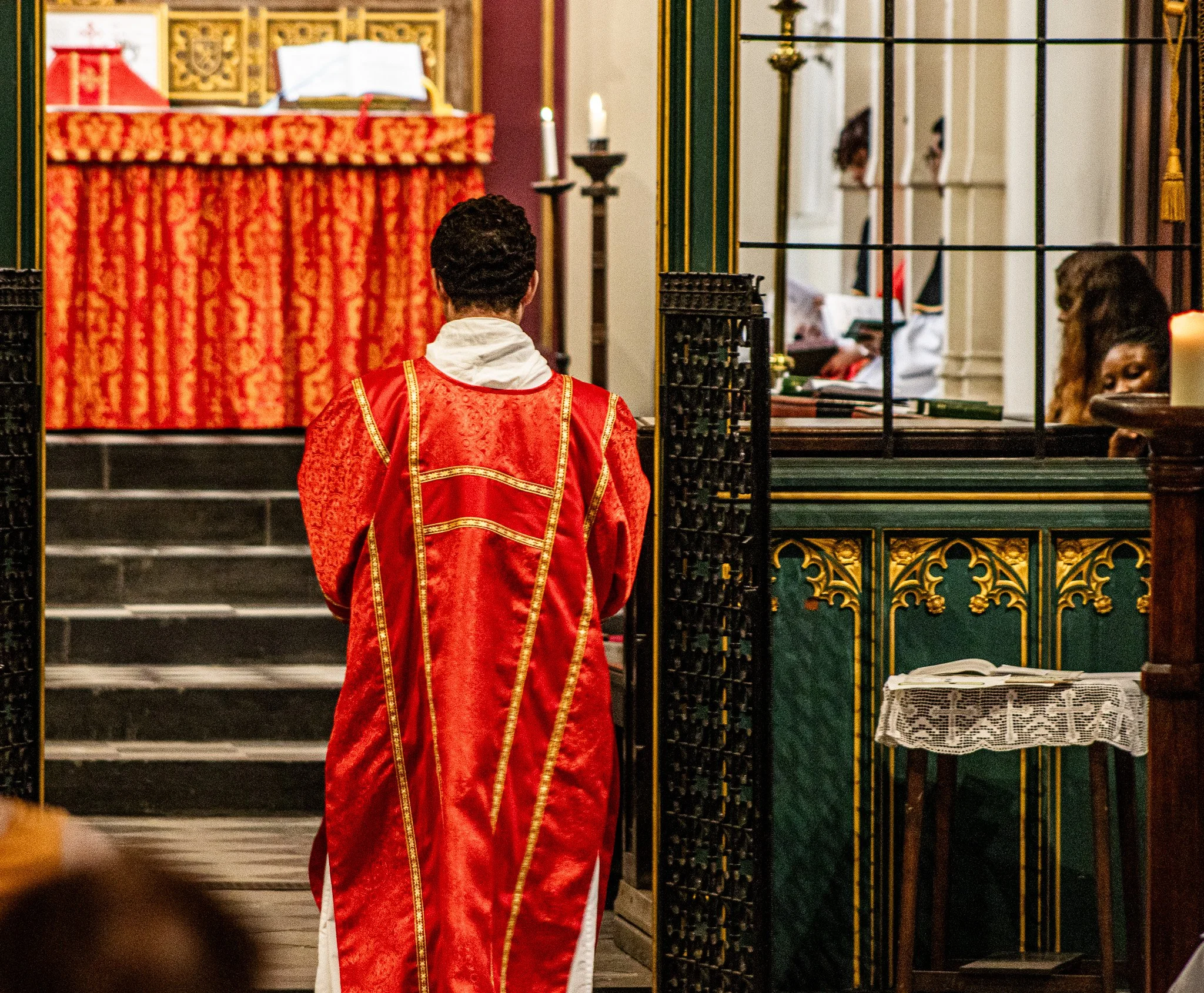 Person in red and gold vestments kneeling before altar inside church.
