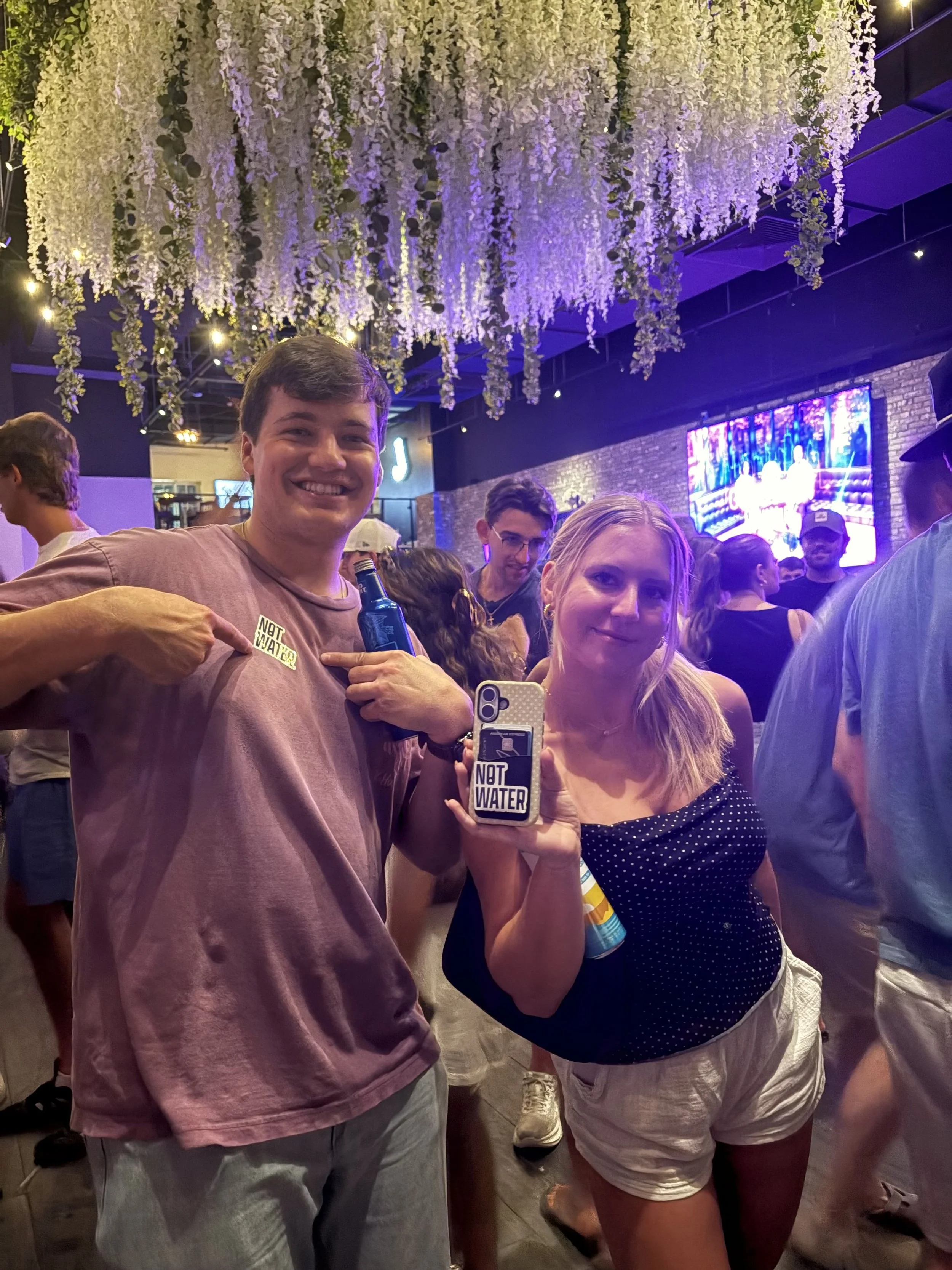 People at a lively social event or party, standing inside a venue and enjoying NOT WATER, a 9% ABV alcoholic beverage with no carbonation, zero sugar, and gluten free ingredients.