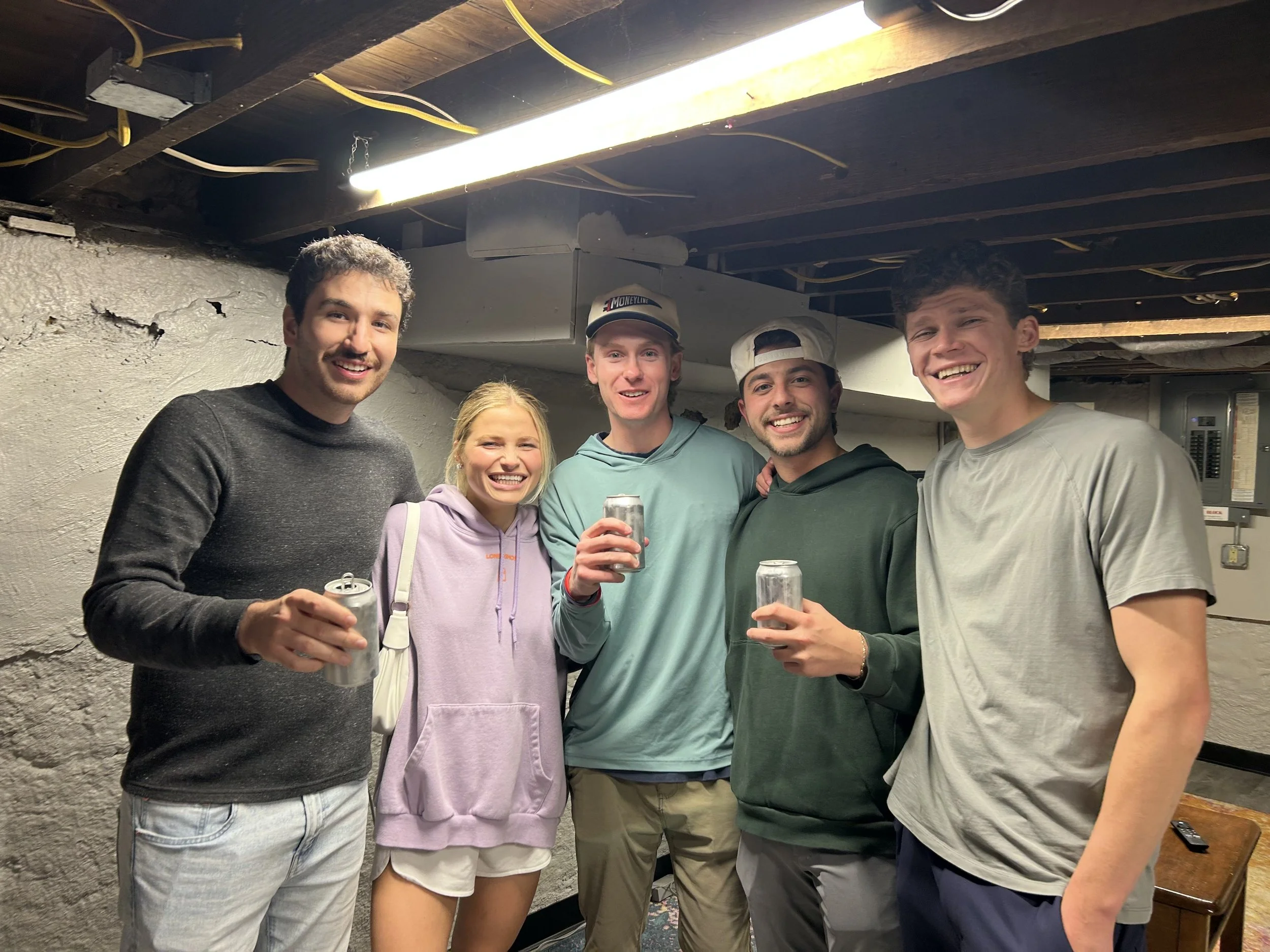 A group of five young adults smiling and holding cans of NOT WATER, a 9% ABV alcoholic beverage with no carbonation, zero sugar, and gluten free ingredients, at the University of Dayton.