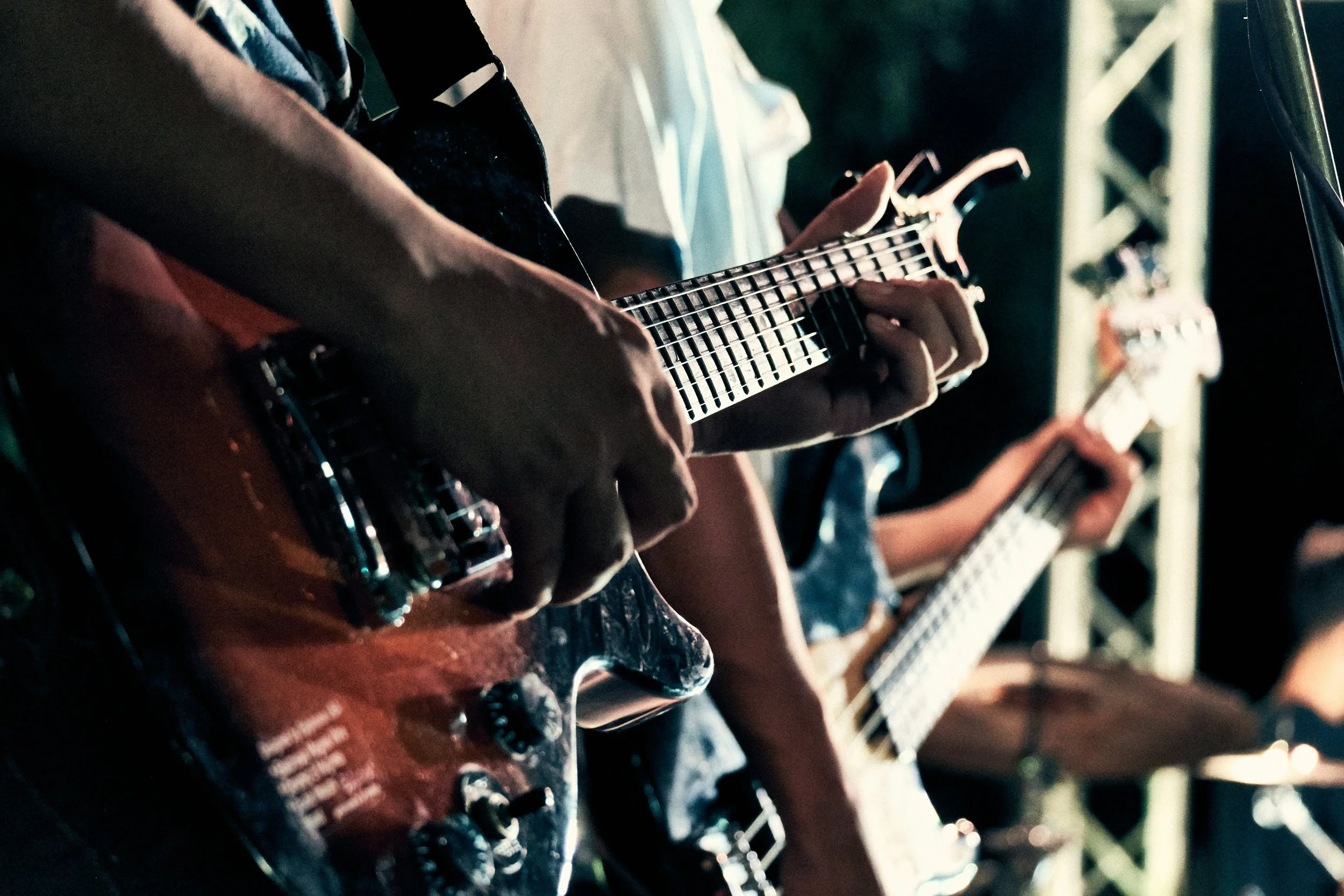 Close-up of multiple hands playing guitars in a band performance, with a focus on strings and fretboards.
