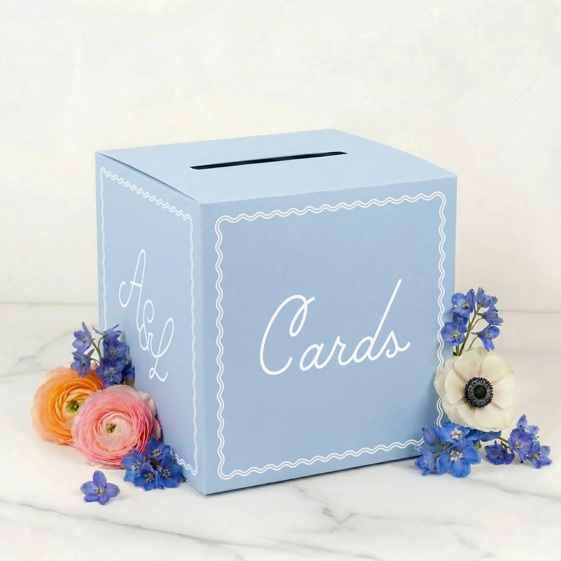 Periwinkle blue box labeled 'Luxe Cards' surrounded by pink, purple, and white flowers on a white surface.