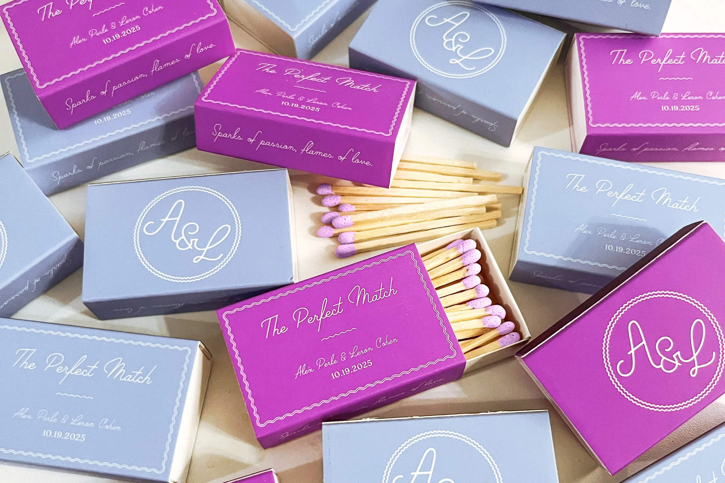 A collection of small, decorative match boxes in pink and periwinkle colors with a white script font. Each box is labeled 'The Perfect Match'. Some boxes are open, revealing pink-tipped matches inside.