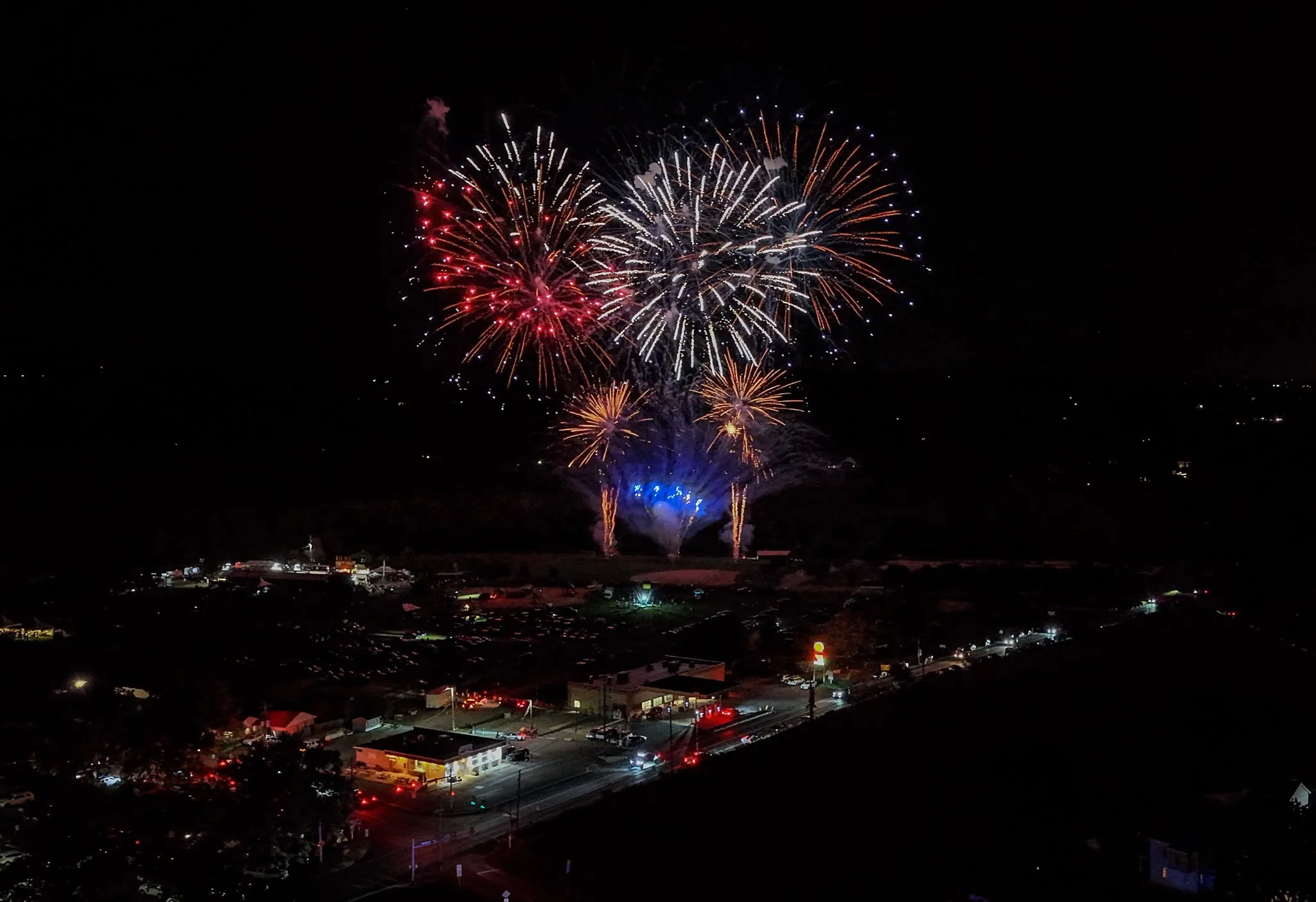 Fireworks exploding in the night sky over a small town, illuminating the area with colorful streaks and bursts.