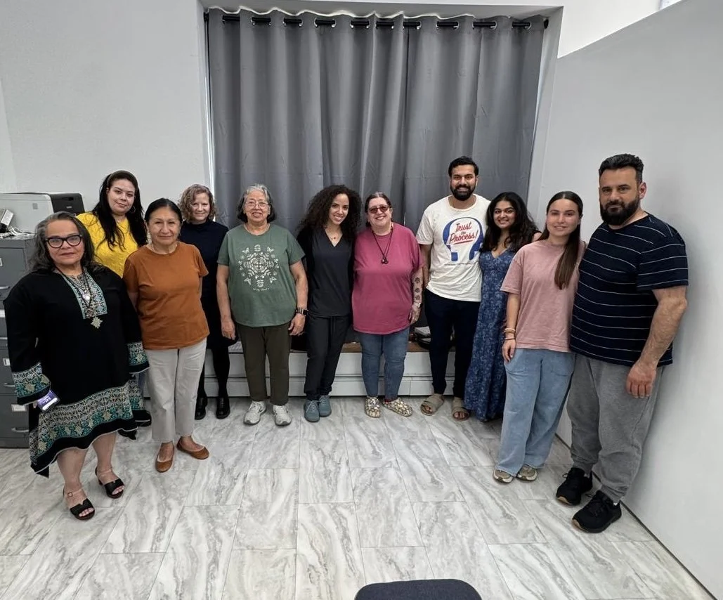 Group of 11 diverse people standing in a room, smiling for the camera after a presentation. The room has a gray curtain and marble floor.