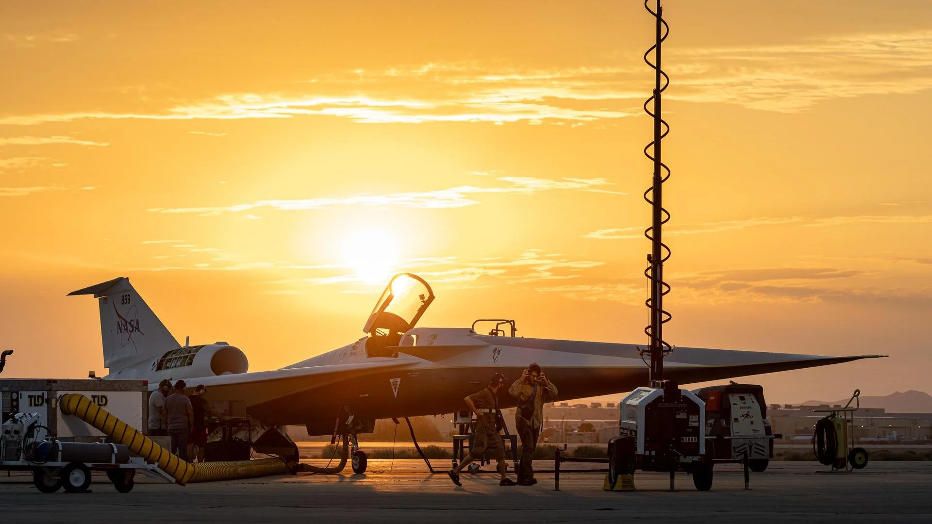 NASA X-59 LBFD on an airport runway during sunset, with ground support equipment and personnel around it.