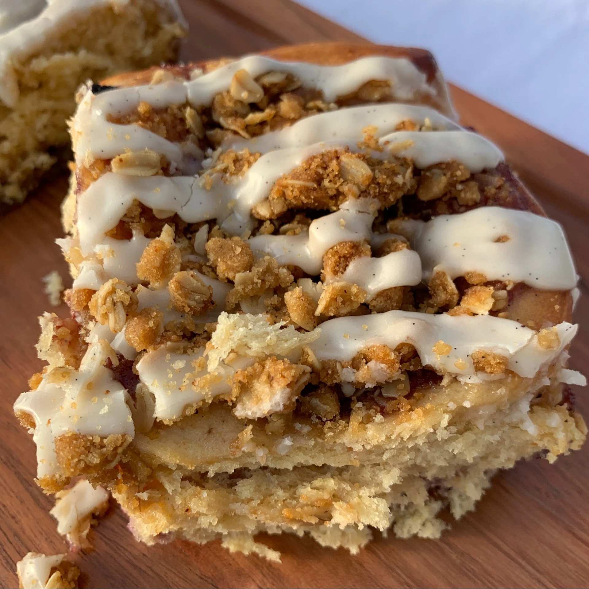 Close-up of a Scroll with apple crisp pie with a crumb topping and drizzled with vanilla icing on a wooden surface.