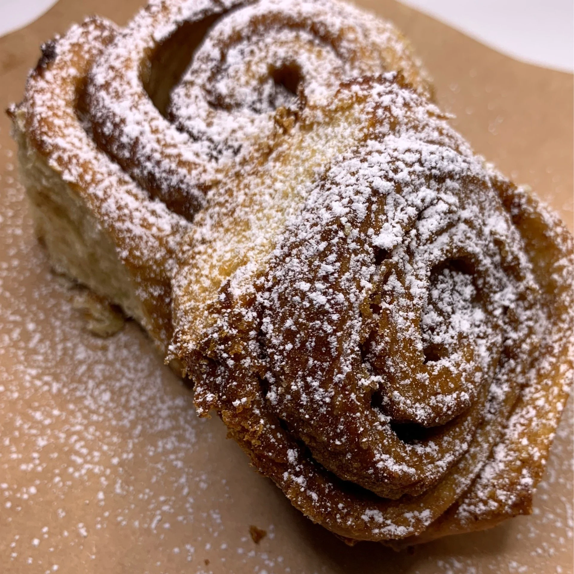 Close-up of cinnamon rolls dusted with powdered sugar on a brown surface.