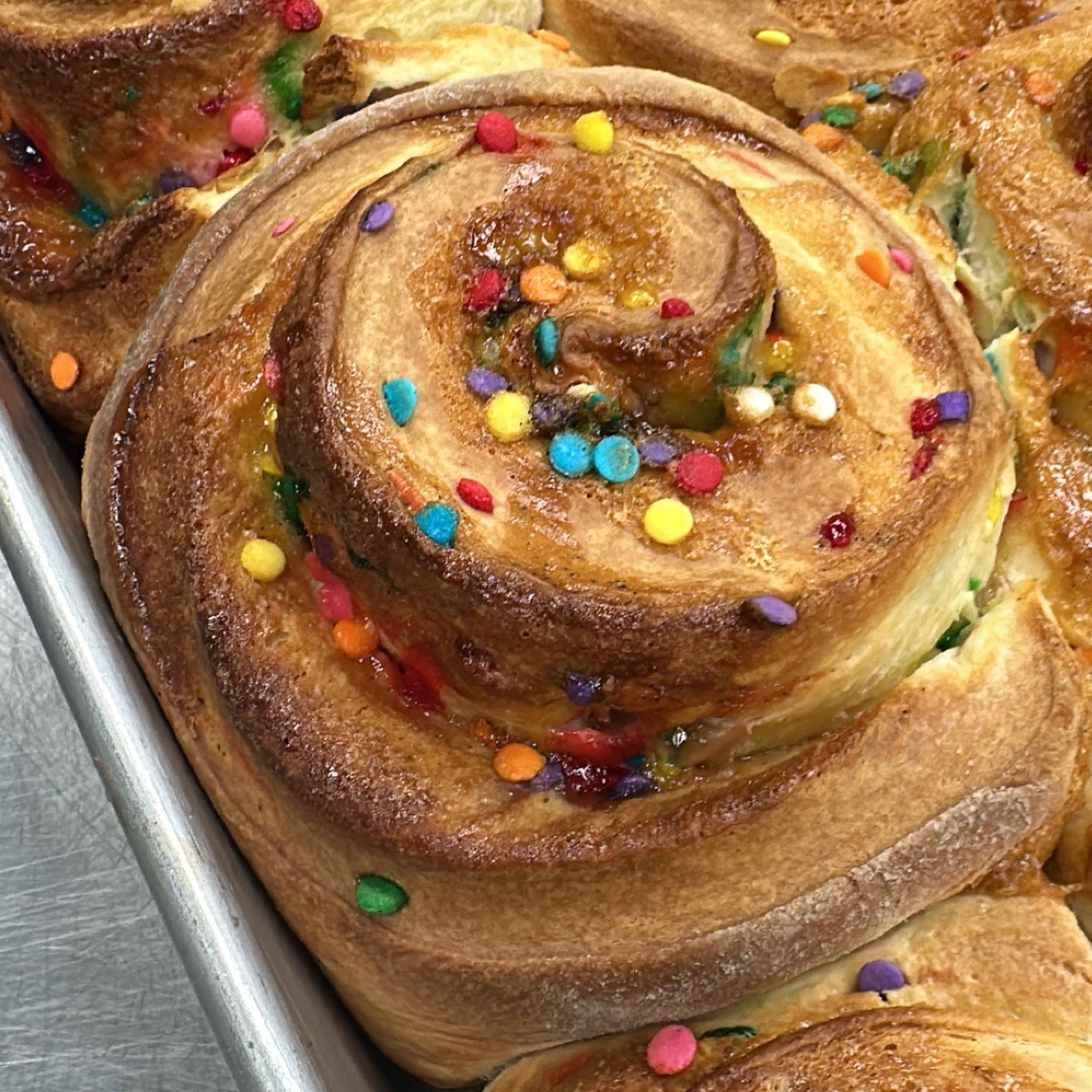 Close-up of a tray of cinnamon rolls decorated with colorful sprinkles.