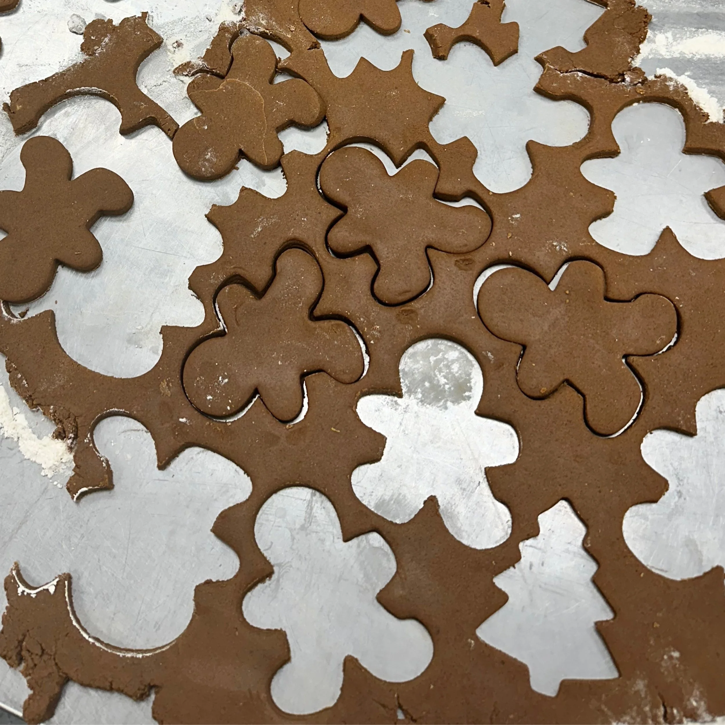 Unbaked holiday cookies cut into various festive shapes on a baking sheet, with some cracks visible in the dough.
