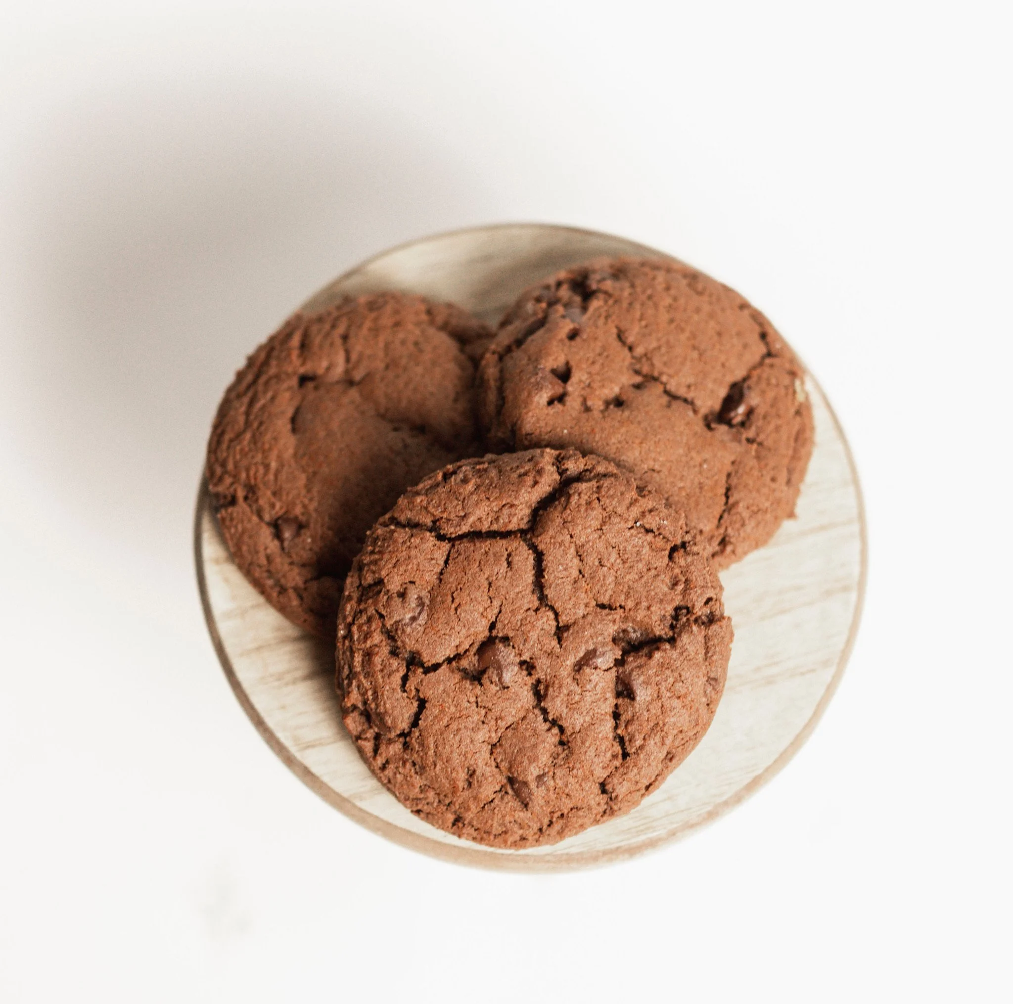 Close-up of three freshly baked chocolate cookies on a white plate with a plain white background.