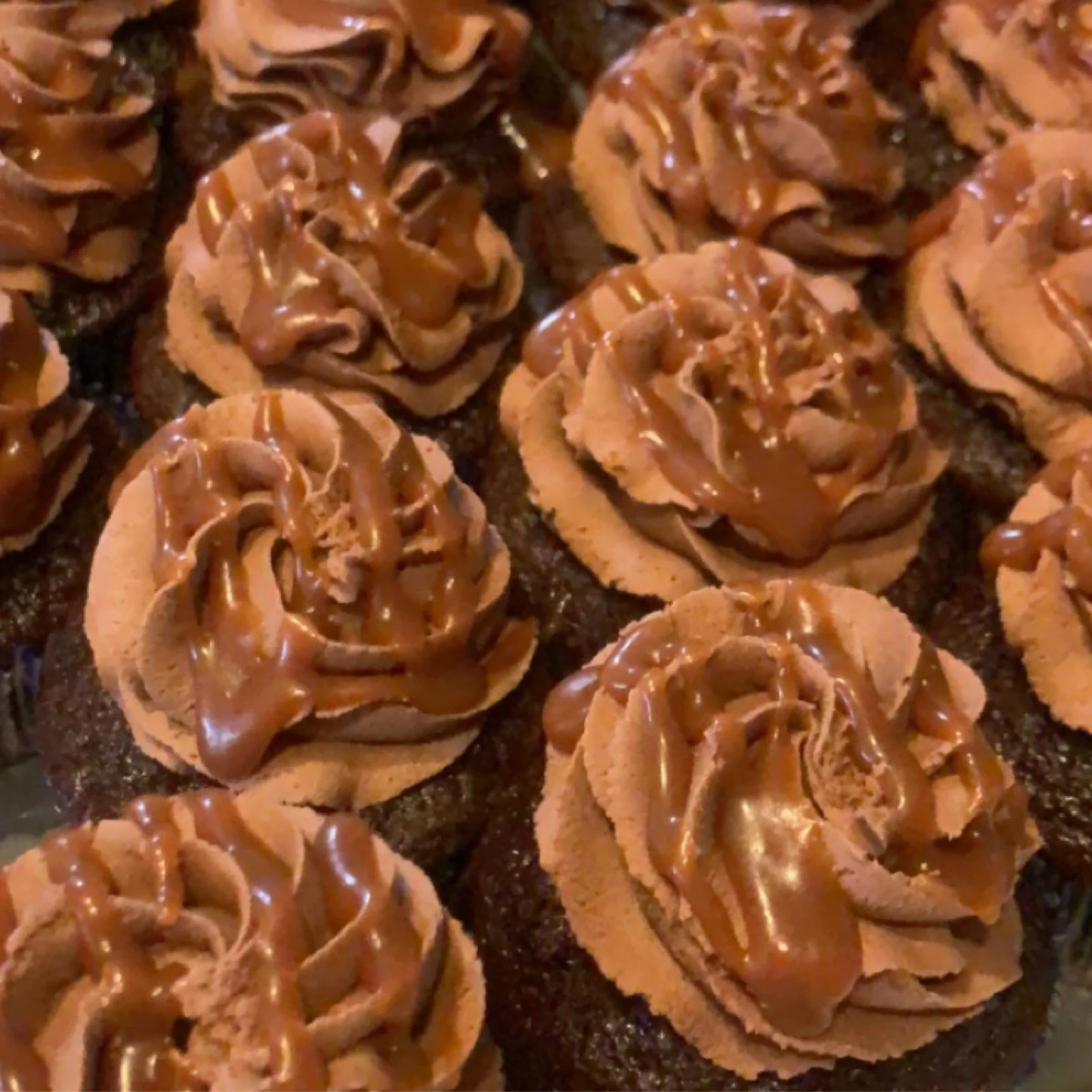 Several chocolate cupcakes with swirled chocolate frosting drizzled with caramel sauce.
