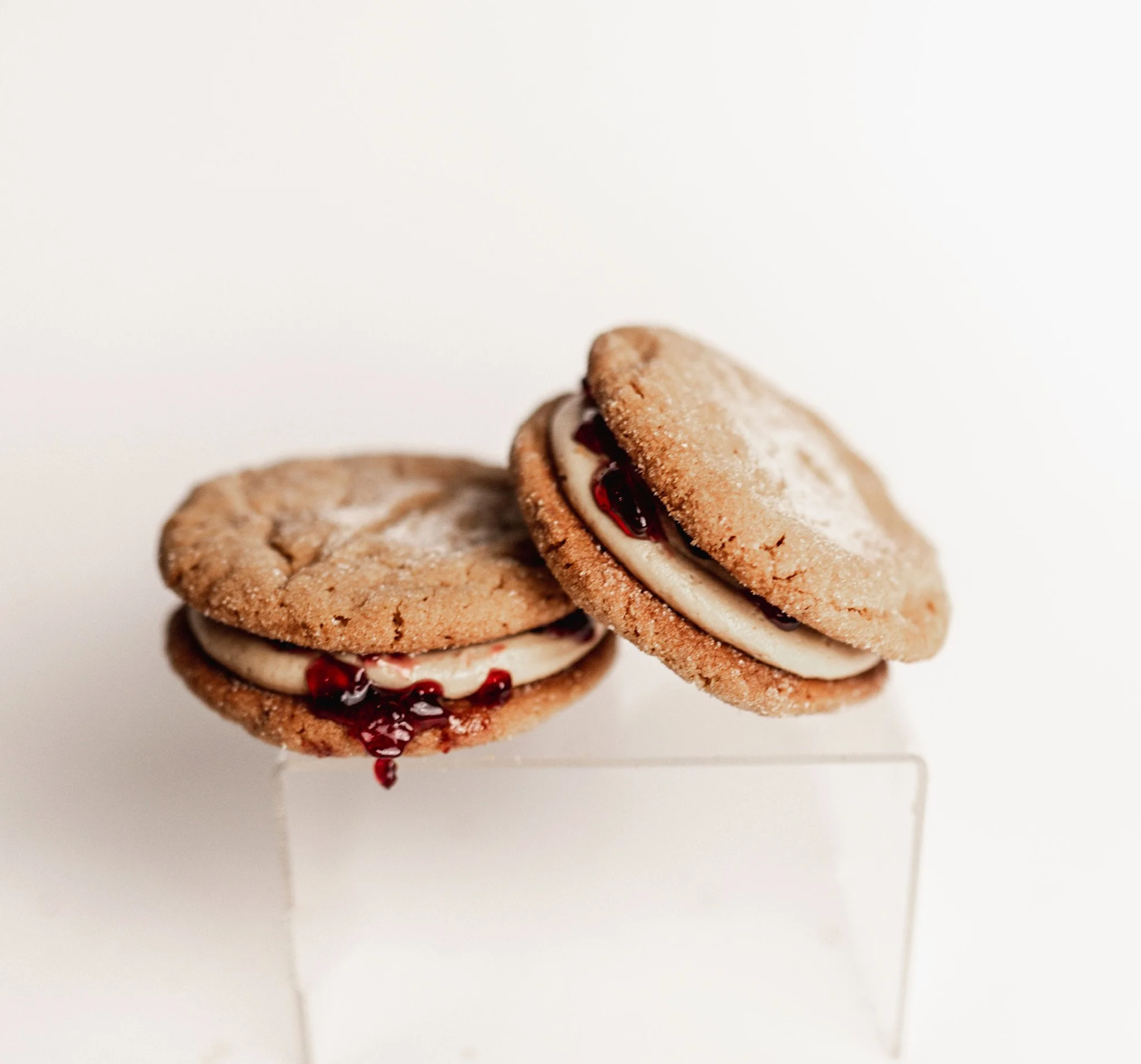 Close-up of two cookies with jam filling, one partially overlapping the other, on a white surface.