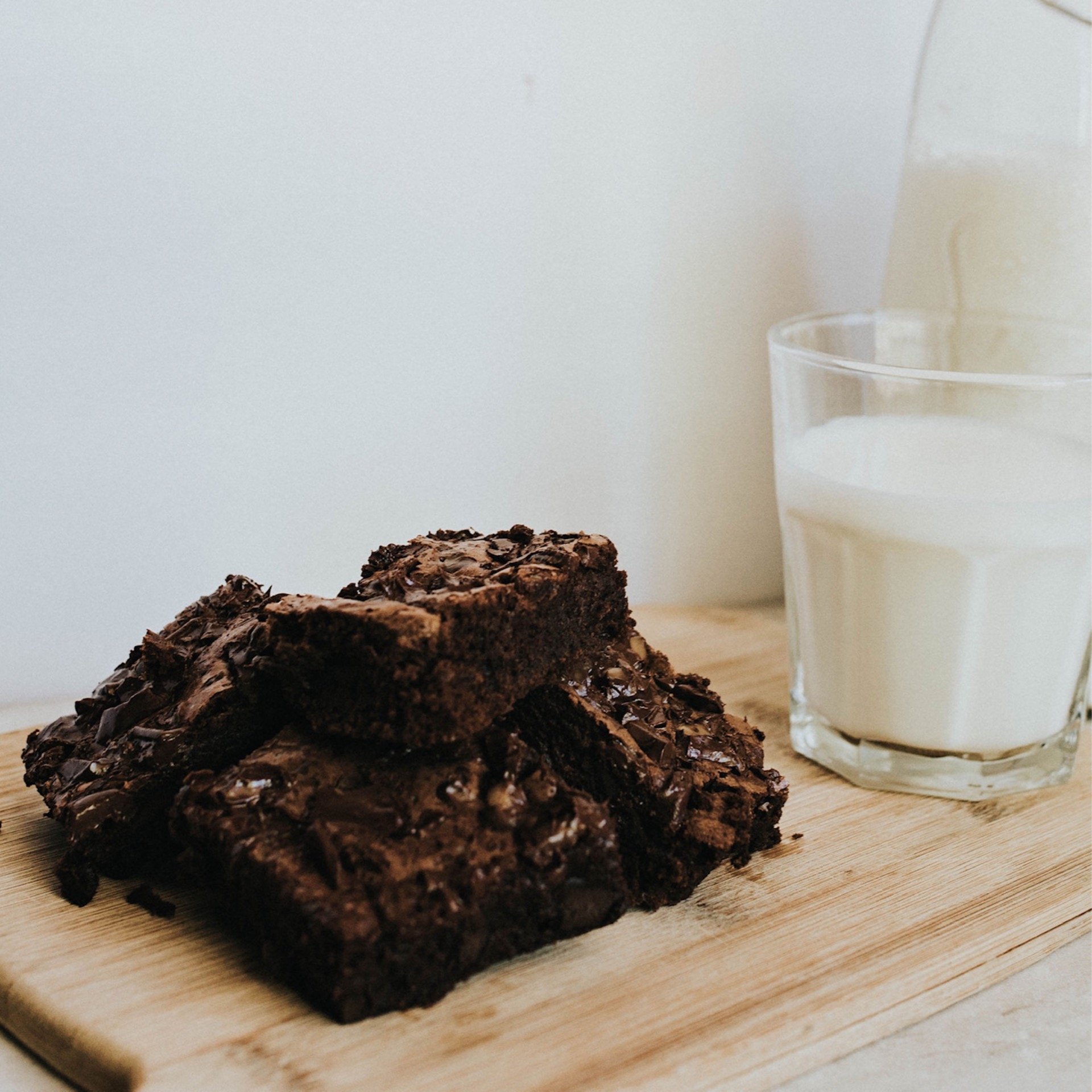 Chocolate brownie on a wooden surface next to a glass of milk.
