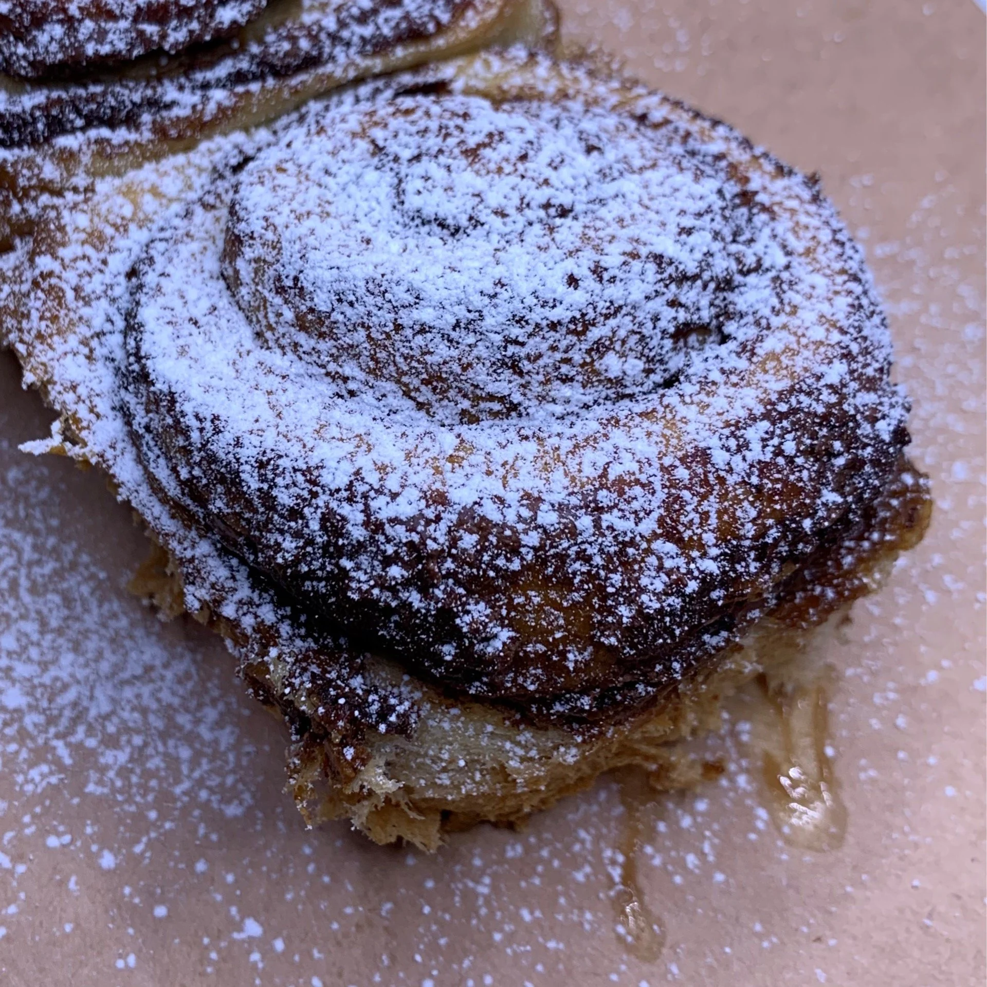 Close-up of a cinnamon roll topped with powdered sugar on a baking sheet.