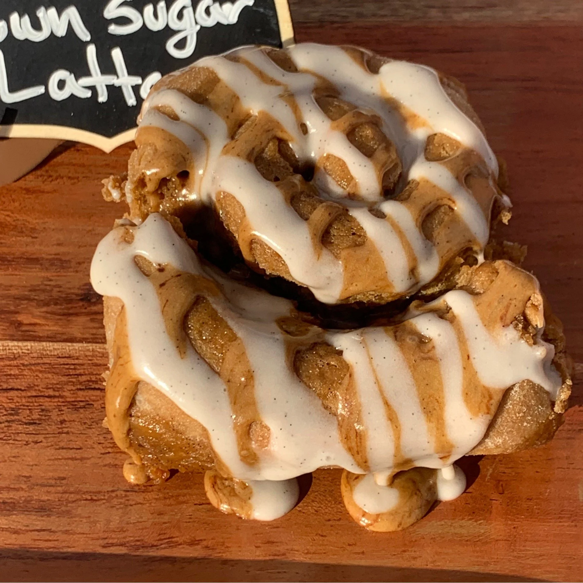 Close-up of a brown sugar latte Scroll with white icing and caramel drizzle placed on a wooden surface.