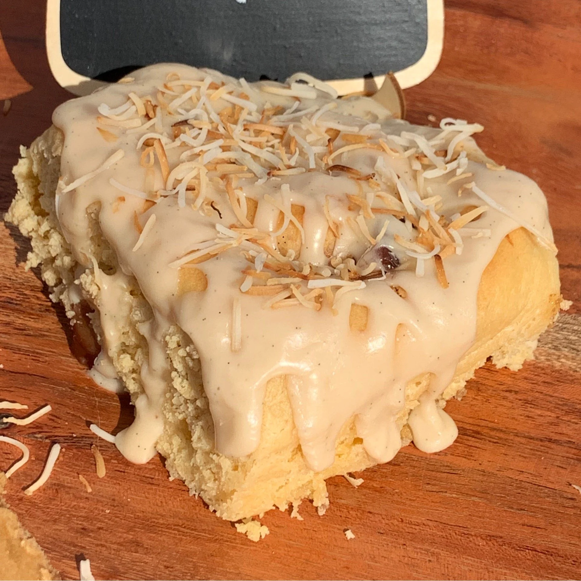 A Scroll topped with white icing and shredded coconut on a wooden surface.