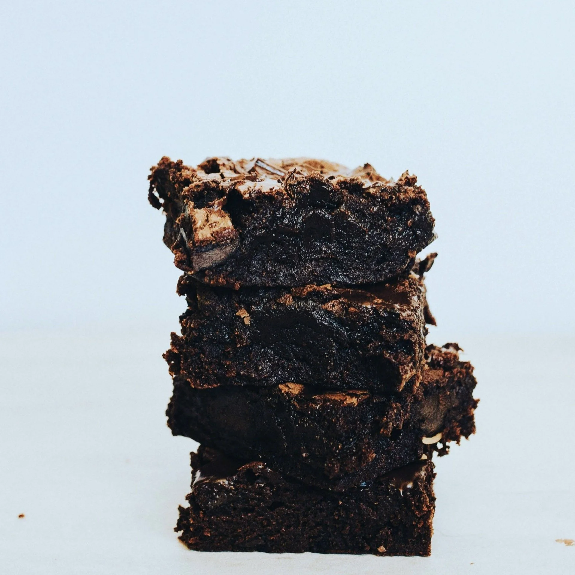 A stack of four chocolate brownies on a white surface with a light blue background.