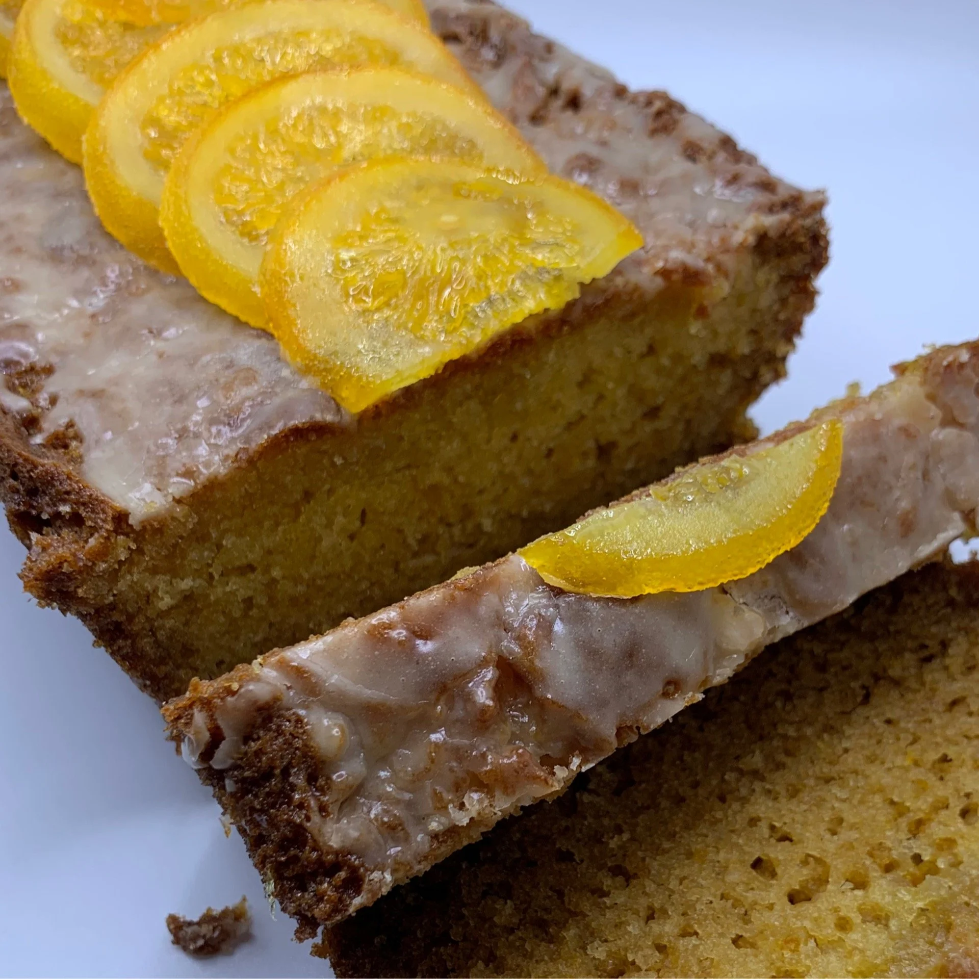 Close-up of a slice of lemon cake with lemon slices on top, topped with white icing, on a white plate.