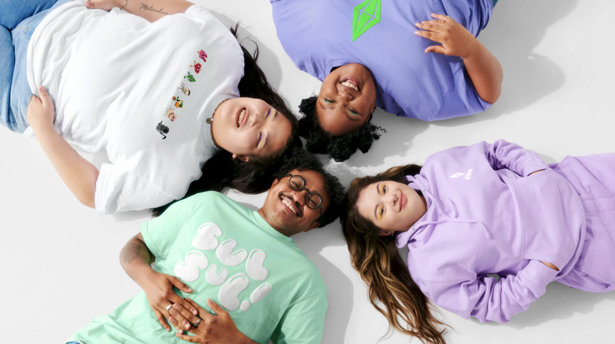 Five diverse friends lying on the white floor, smiling and looking up, dressed in colorful casual clothes.
