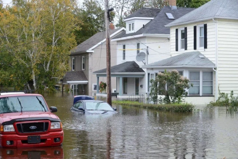 Flooded residential street with partially submerged cars and houses.