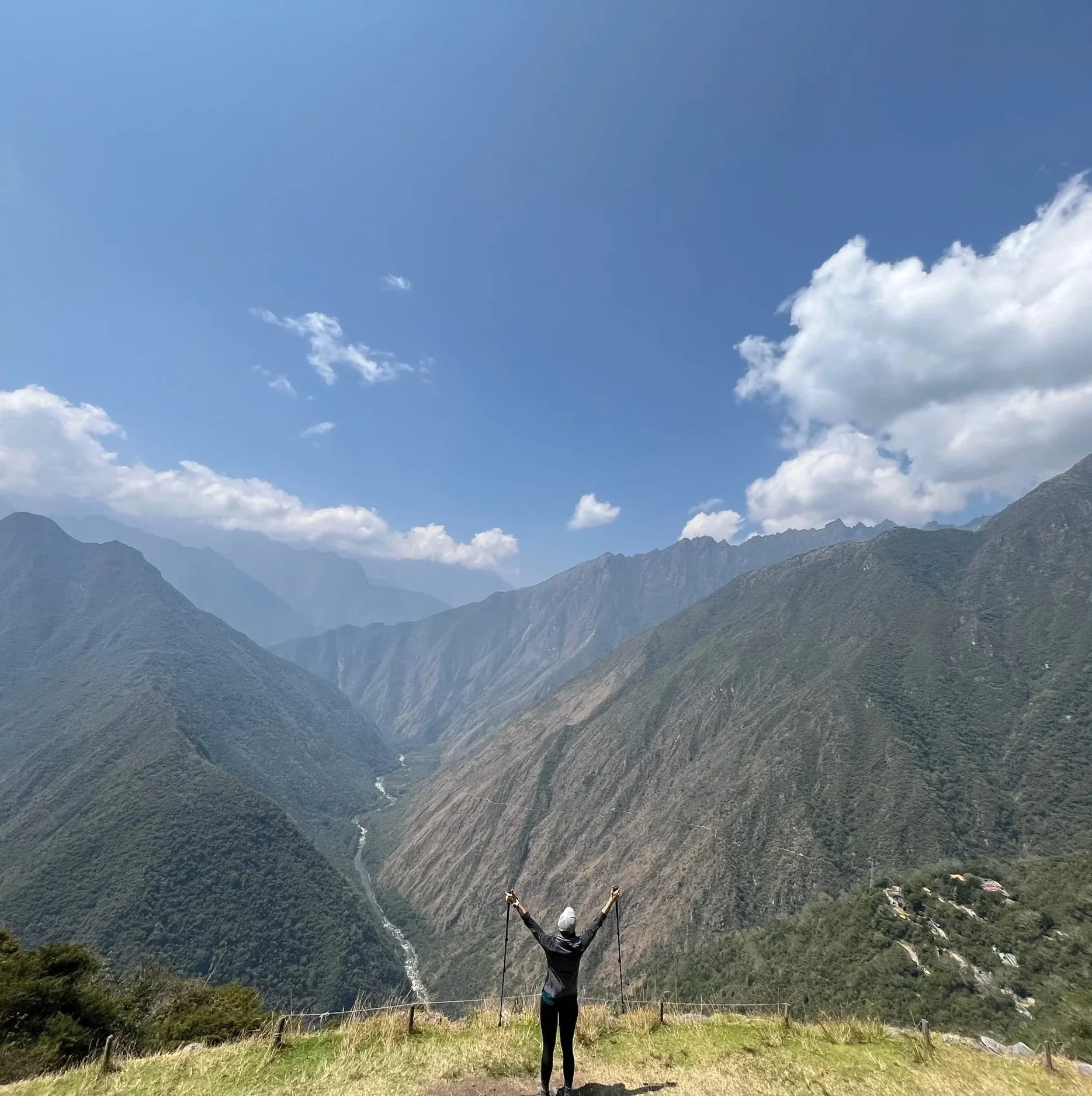 Person standing on a mountain overlook surrounded by a dramatic green valley, representing adventure, vitality and healthy living.