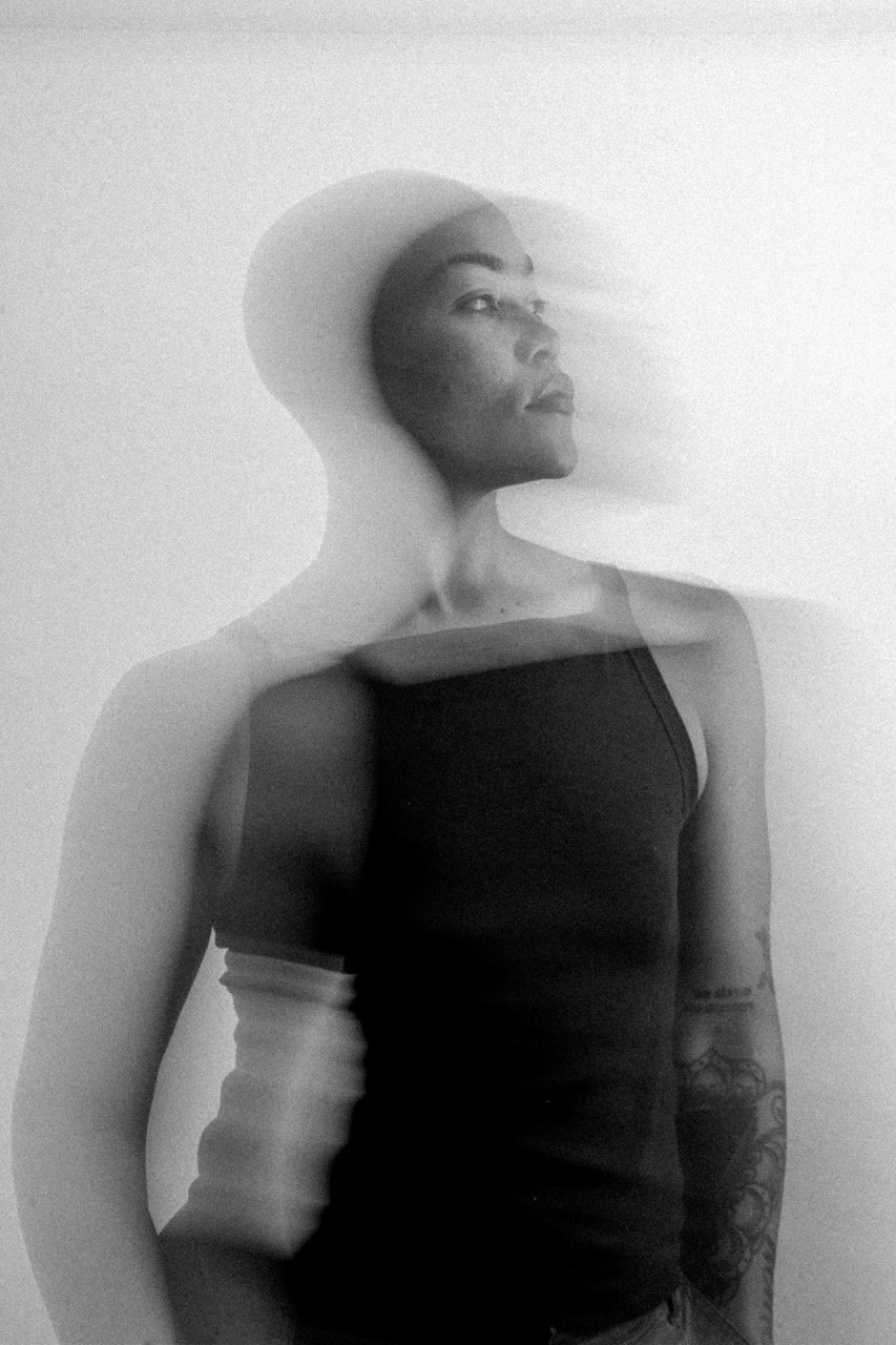 Black and white photo of a woman in a tank top, with a double exposure or motion effect creating a ghostly, layered appearance.