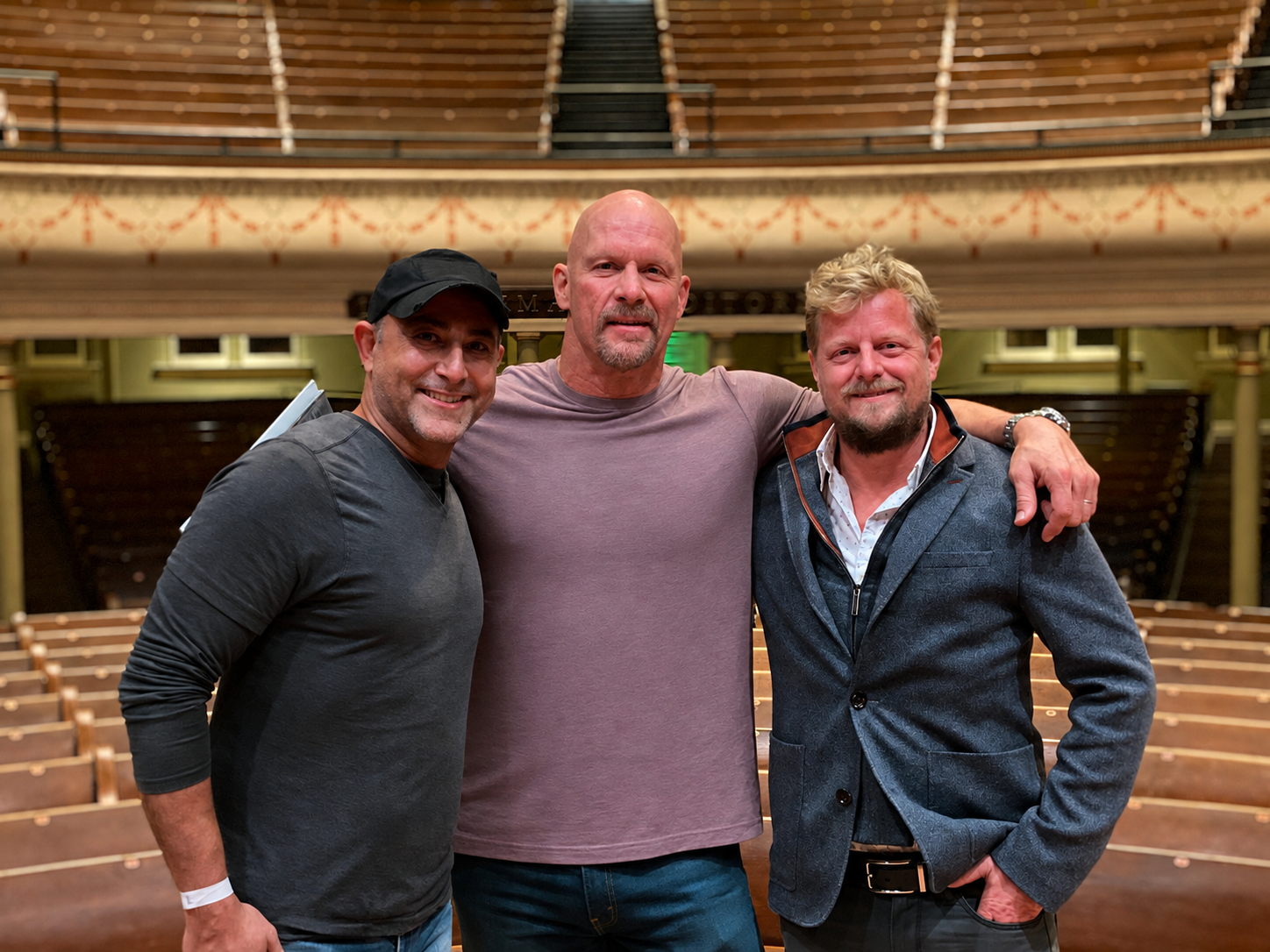 Steve Austin with the producers standing together in an auditorium, smiling at the camera.